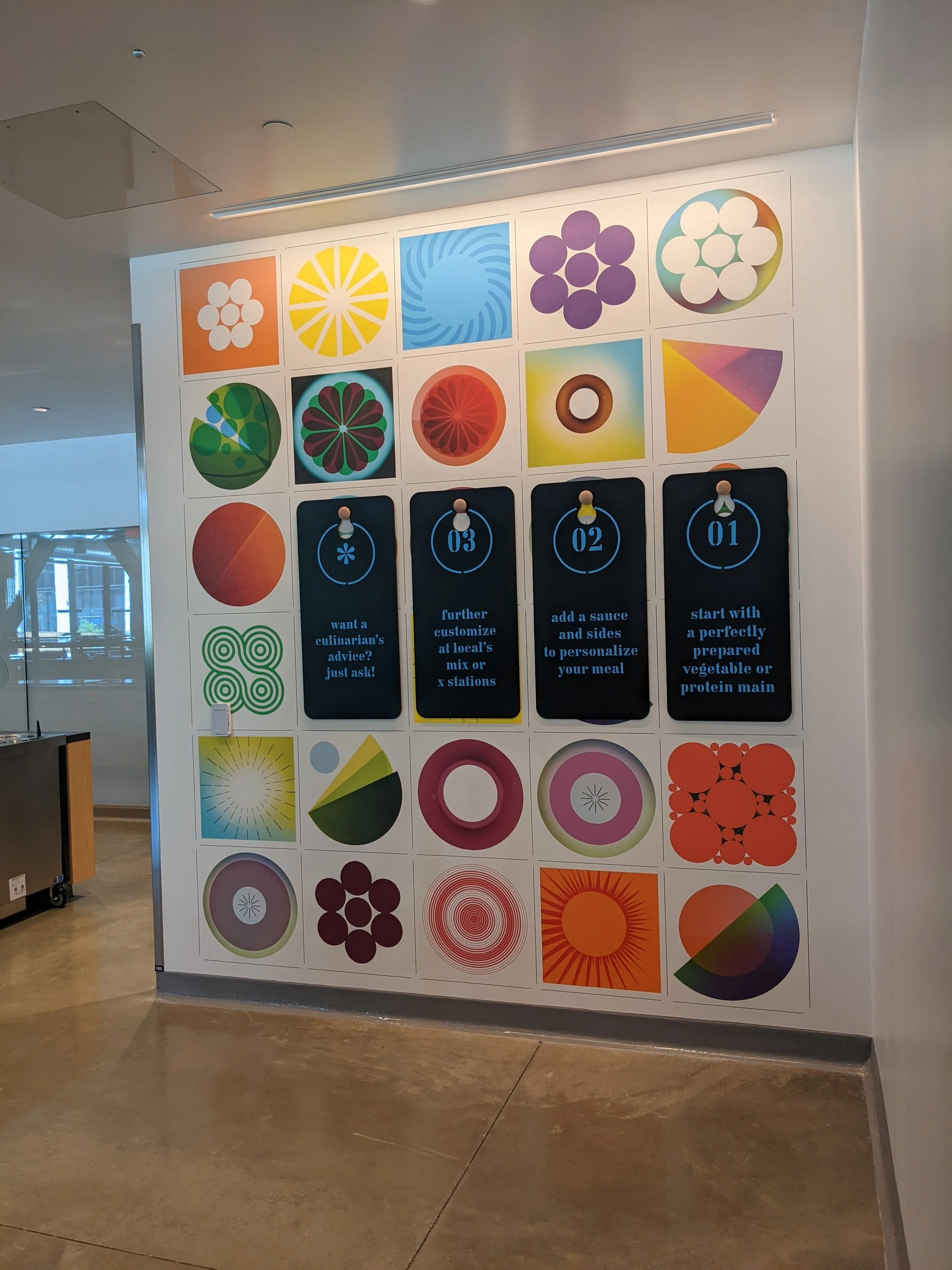 Close-up of custom environmental wall graphics with branded messaging and wayfinding panels integrated into colorful geometric wallcovering in commercial dining space