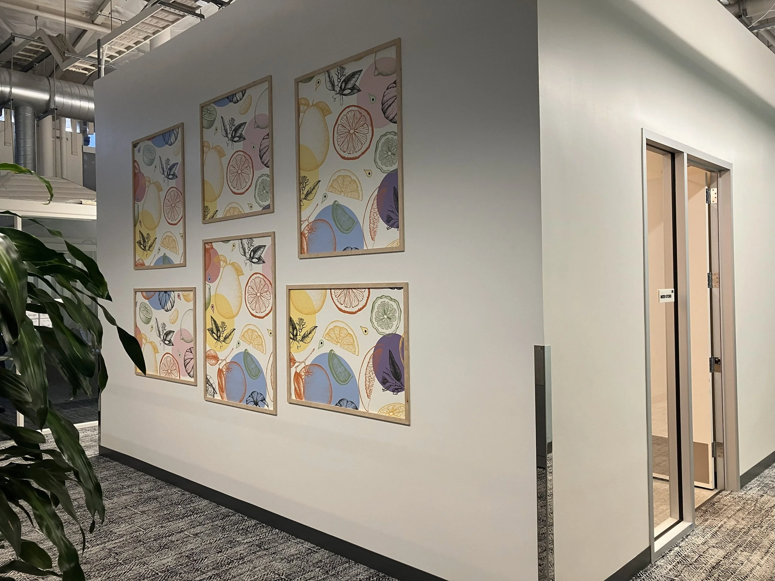 Framed fruit-pattern wallcovering panels installed in a grid layout along an amphitheatre hallway wall, creating a colorful environmental graphics display.