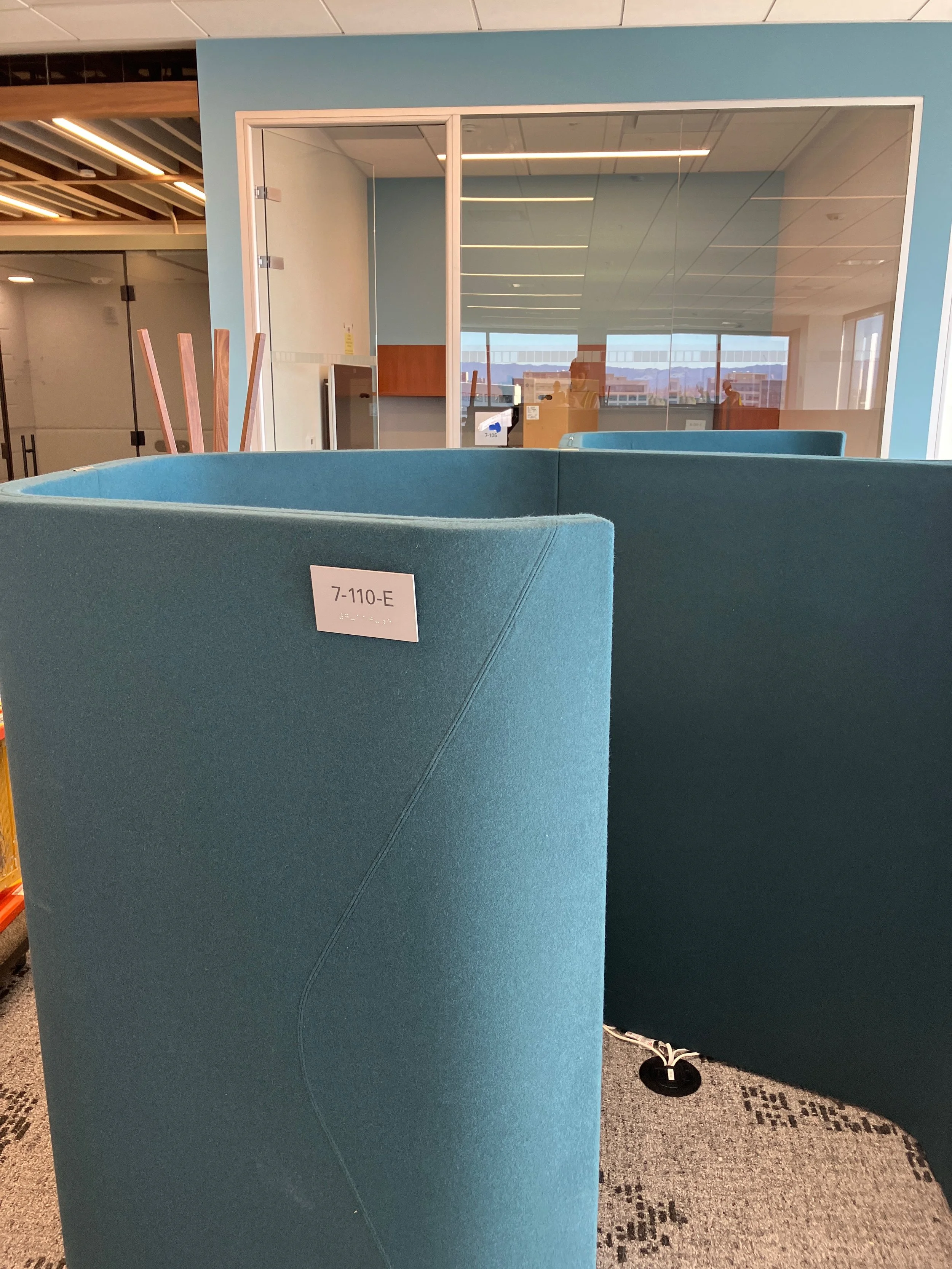 ADA-compliant room identification sign with braille mounted on acoustic privacy pod at the KPMG San Jose office.