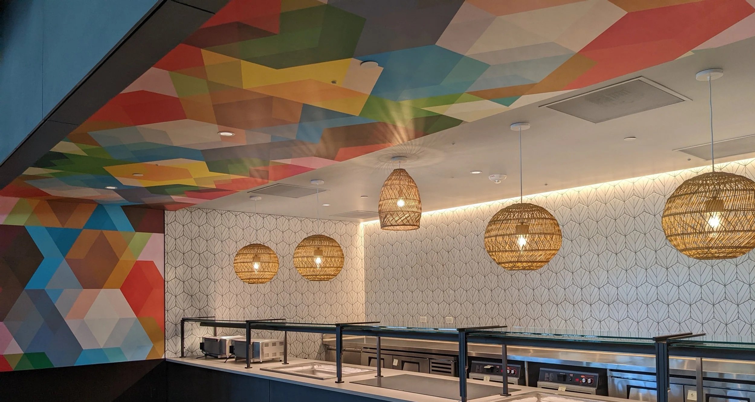 Custom geometric wallcovering and colorful ceiling graphic installation in a modern restaurant interior with decorative lighting and branded environmental graphics