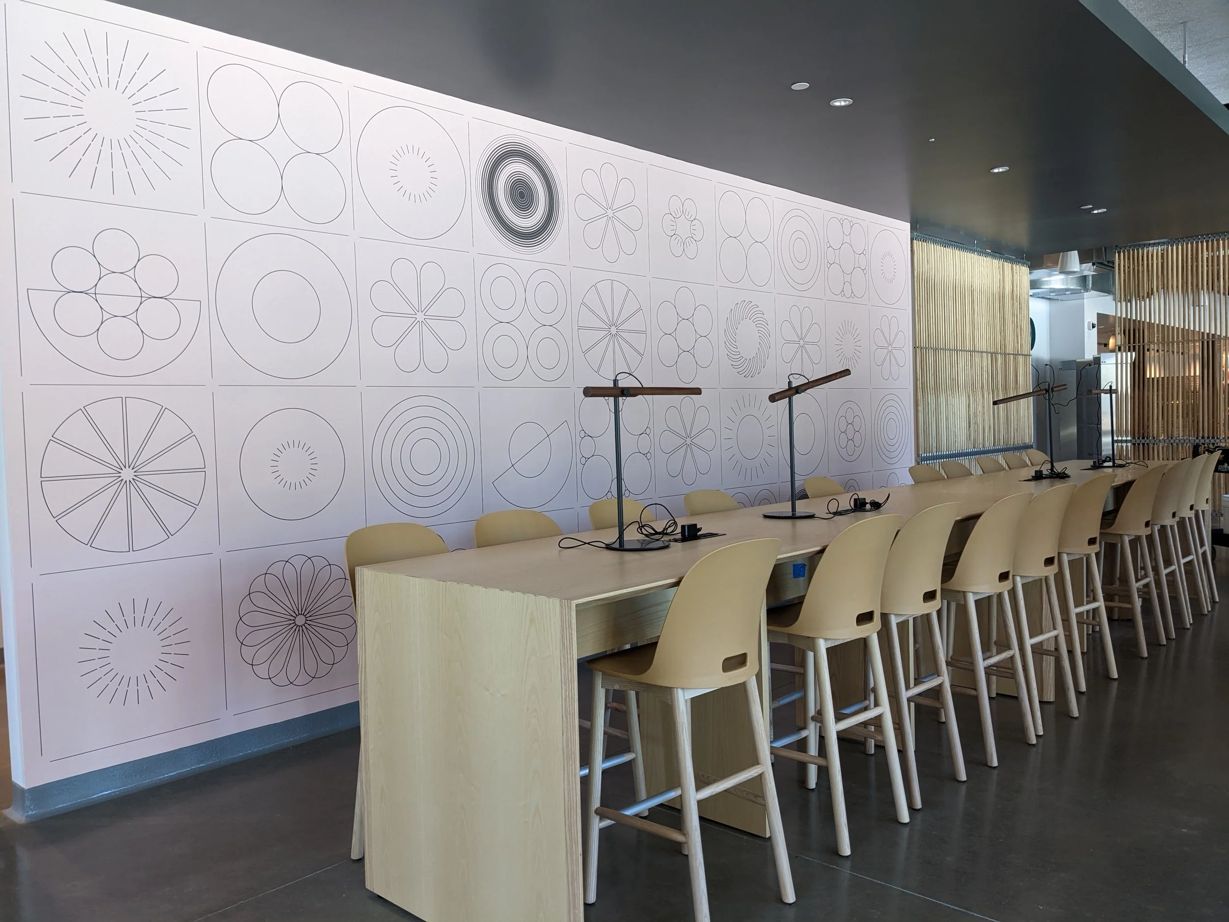 Custom geometric pattern wallcovering installed in a commercial breakroom with shared workspace seating and integrated environmental graphics