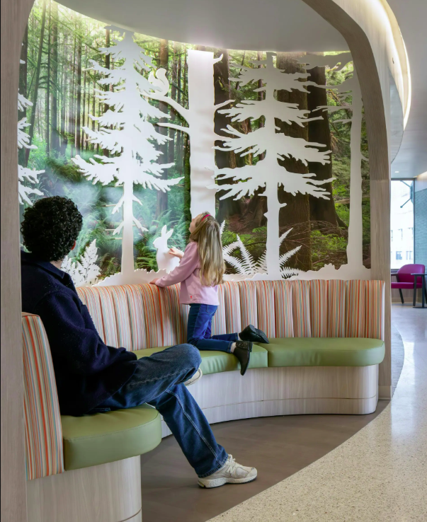 Forest-themed wallcovering with layered tree silhouettes and integrated seating at UCSF Stad Center, creating a biophilic pediatric healthcare environment that supports a calming patient and family experience.