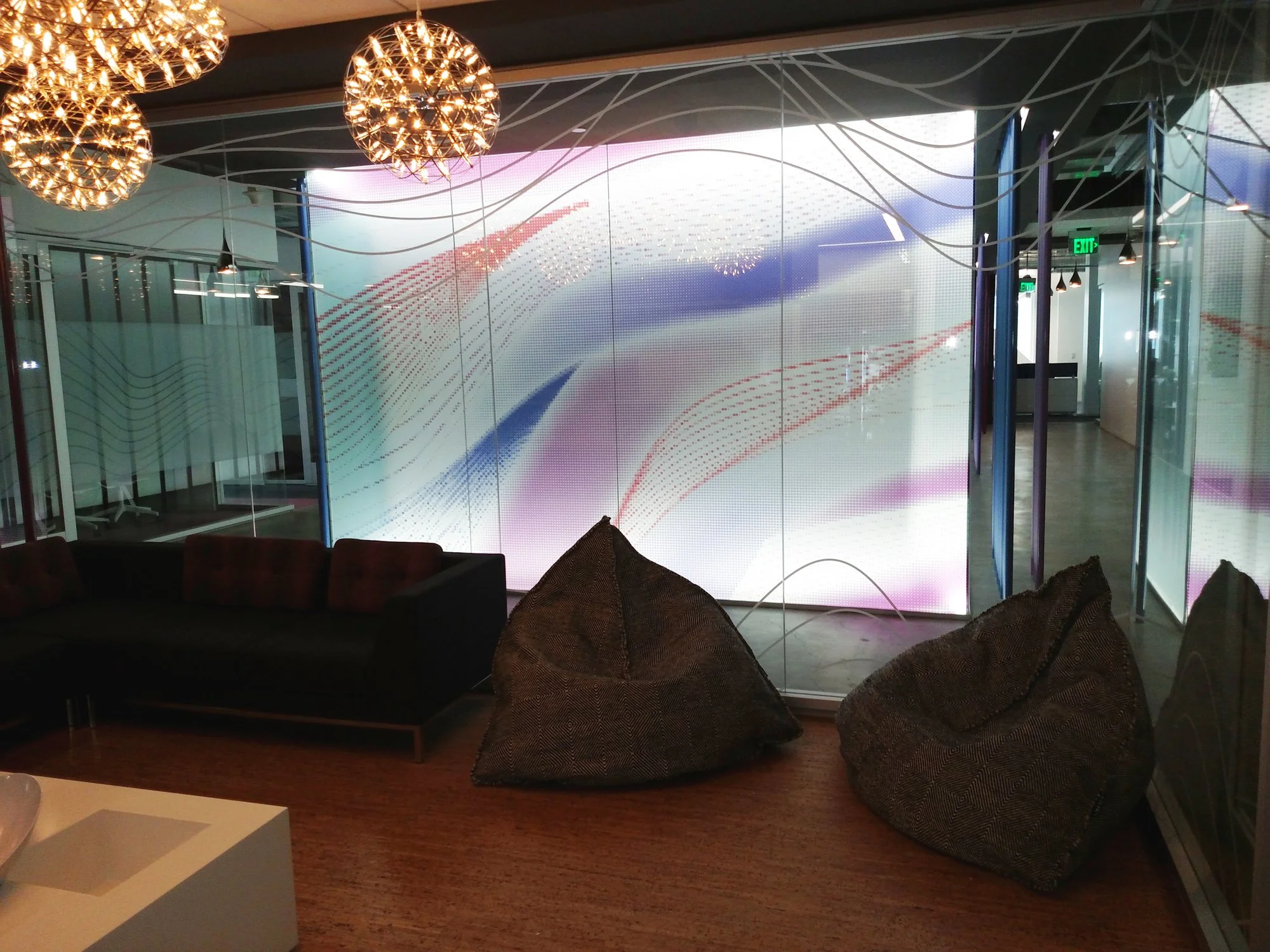 Custom decorative window film with flowing graphic pattern installed on glass wall in a creative office lounge.
