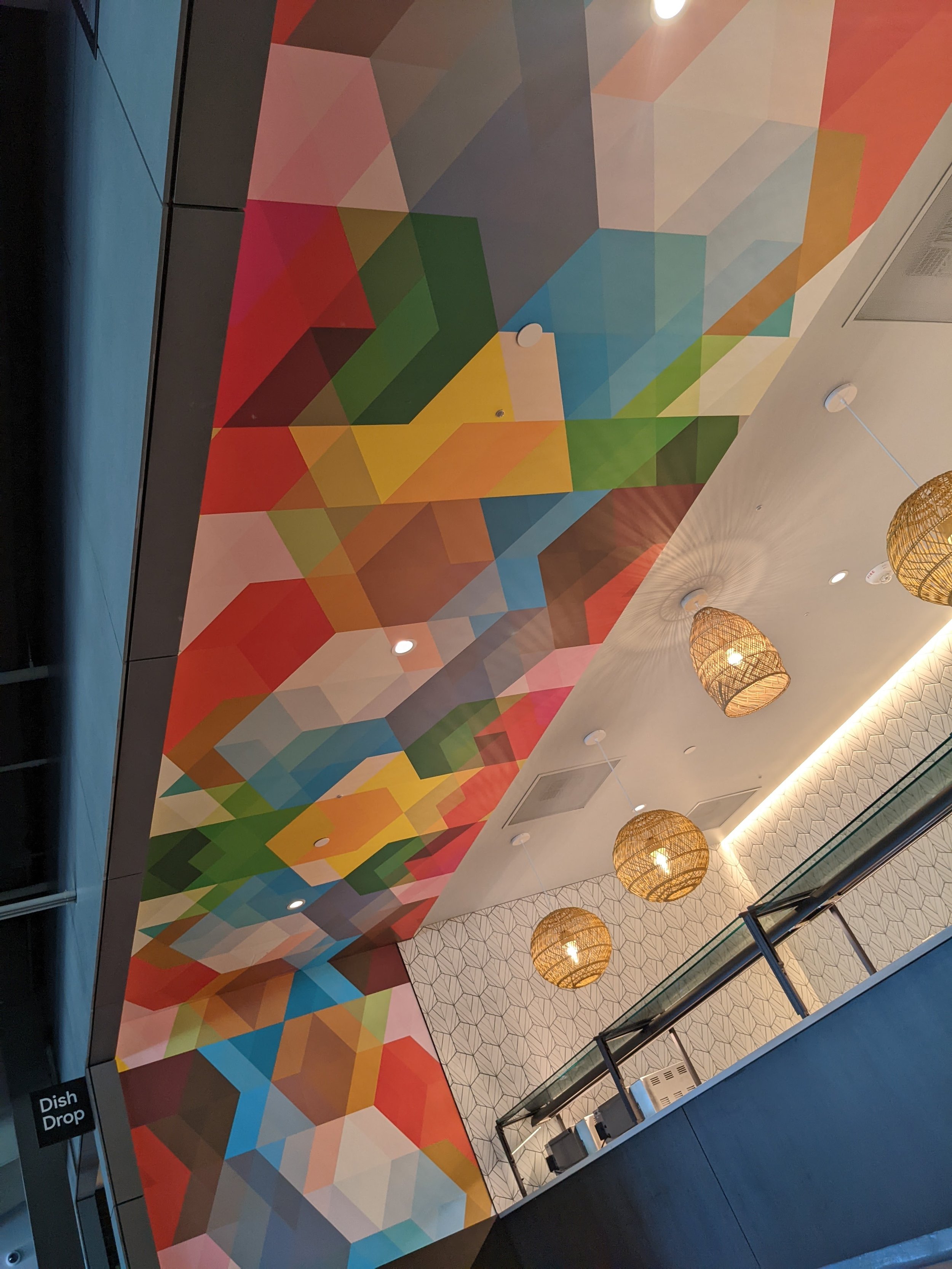 Close-up of vibrant geometric ceiling mural installation in a commercial restaurant interior with custom environmental graphics and decorative lighting