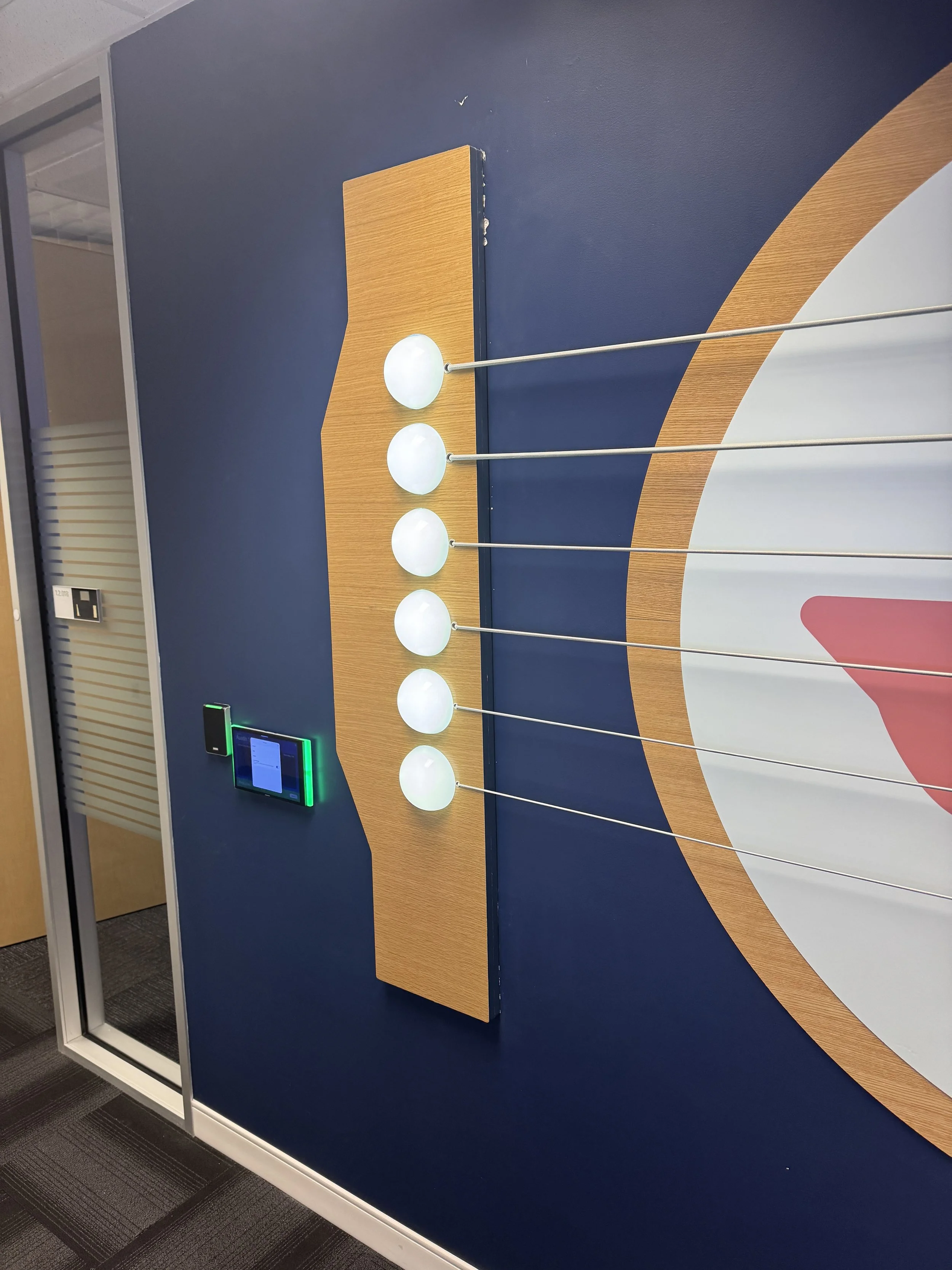 Close-up installation of eBay Austin feature wall showing custom white oak guitar element with LED dome lights and steel cable details integrated into dimensional environmental signage.