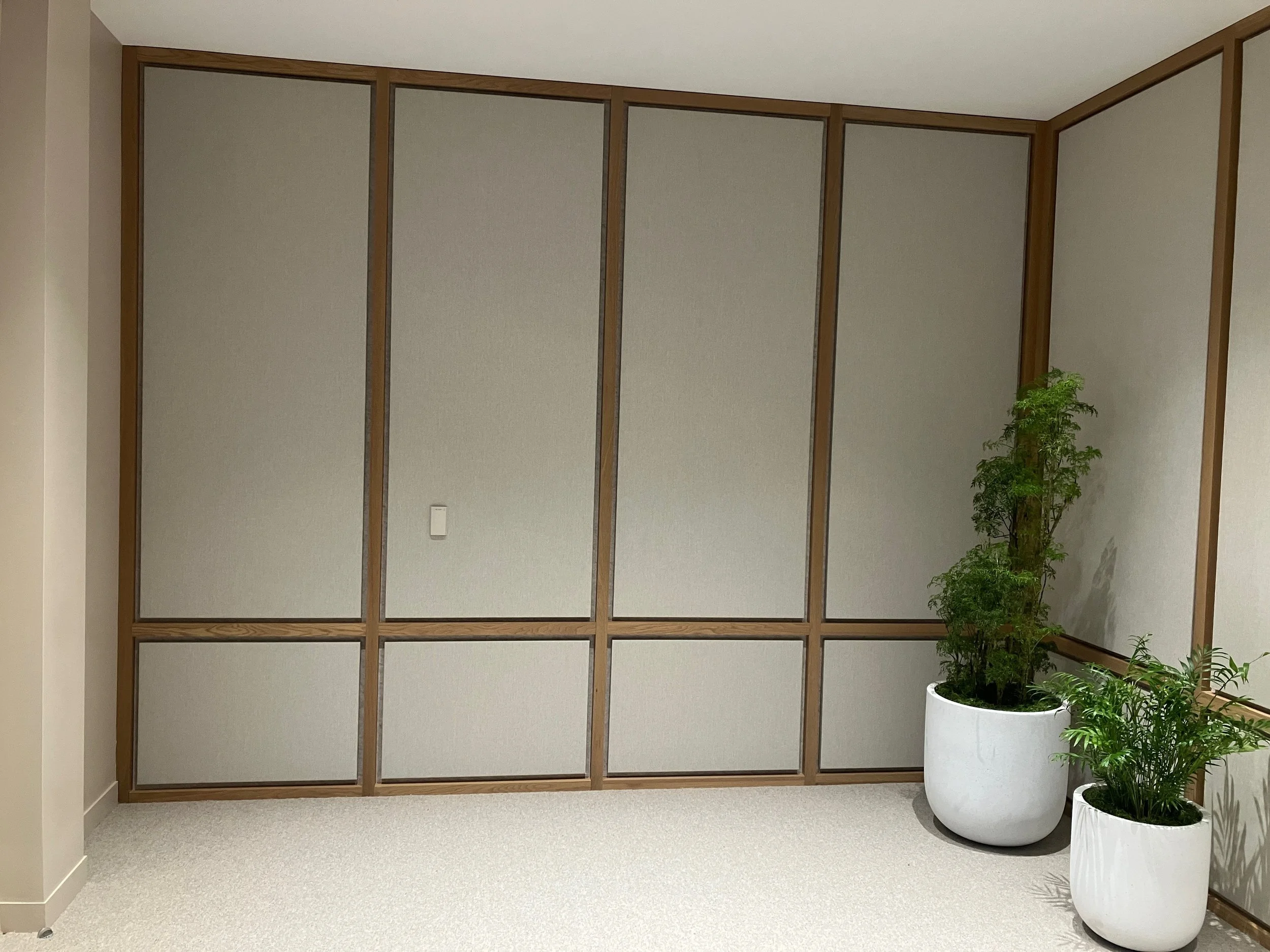 Fabric-wrapped acoustic wall installation with wood detailing designed to reduce echo and improve acoustic comfort in office and meeting environments.