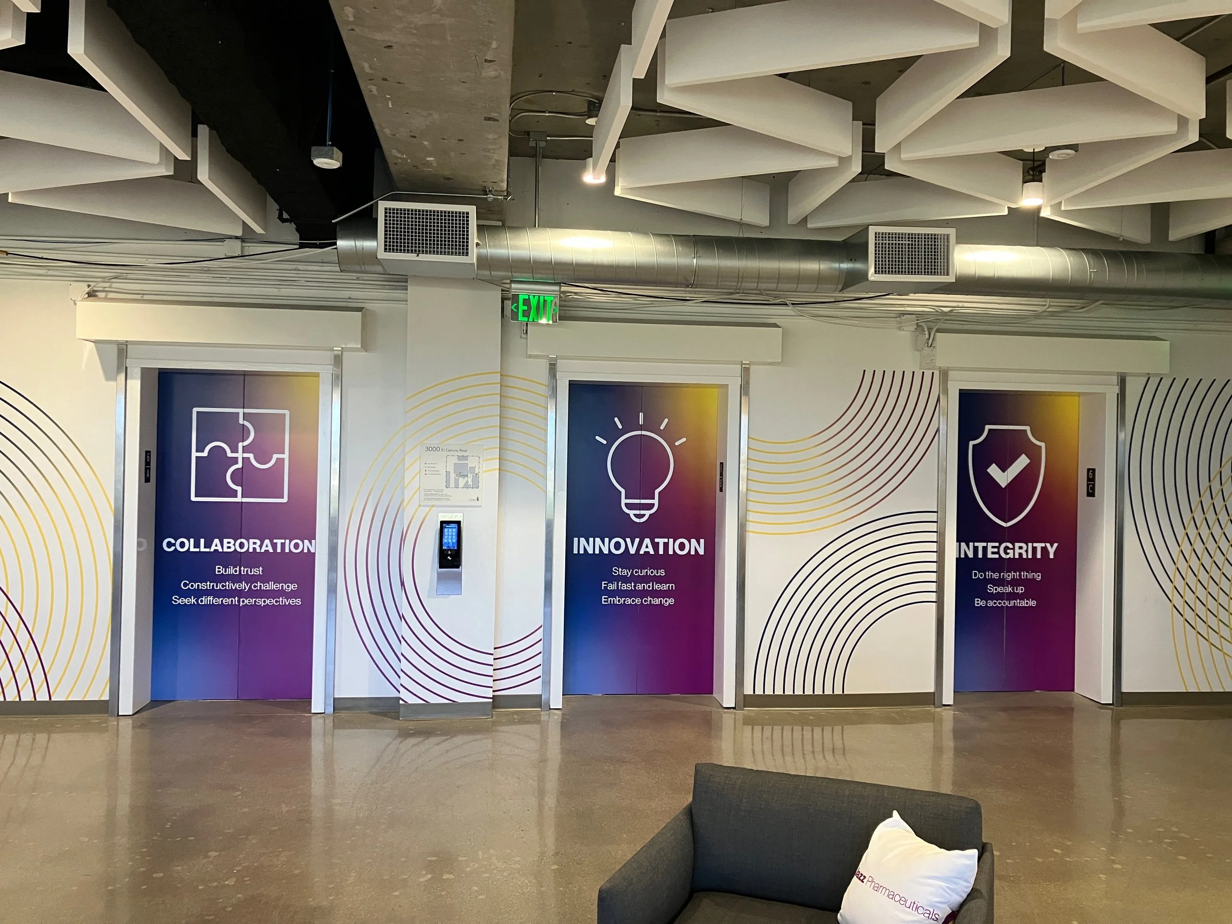Second-phase installed elevator lobby environmental graphics with branded wallcovering and messaging across multiple elevator doors in a commercial office.