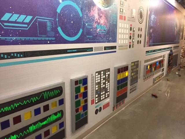Full-scale experiential wall installation combining graphics, dimensional elements, and lighting to simulate a high-tech environment.