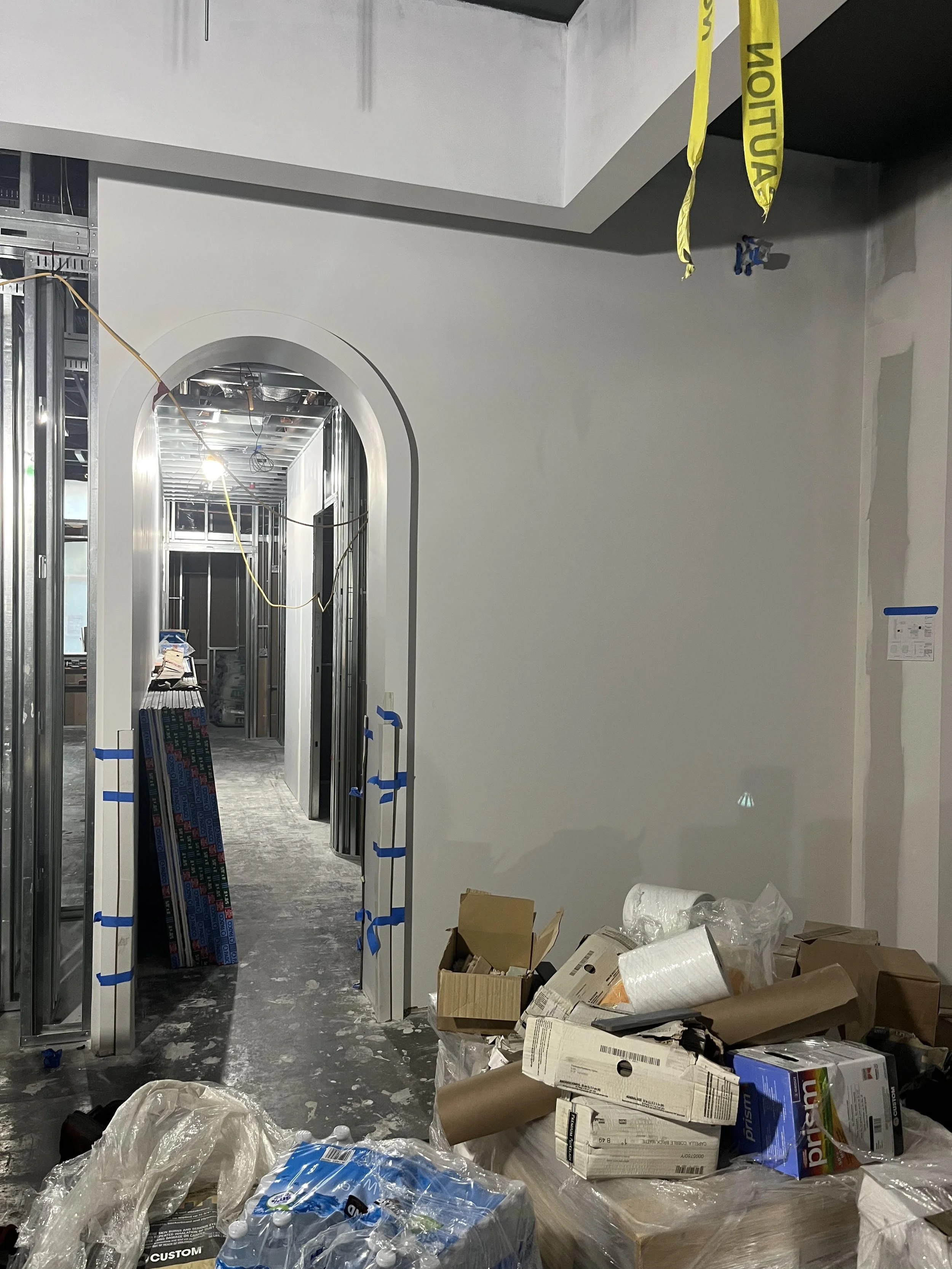 Commercial interior corridor under construction with newly finished drywall walls, door framing, and electrical rough-in, prepared for final finishes and graphics installation.