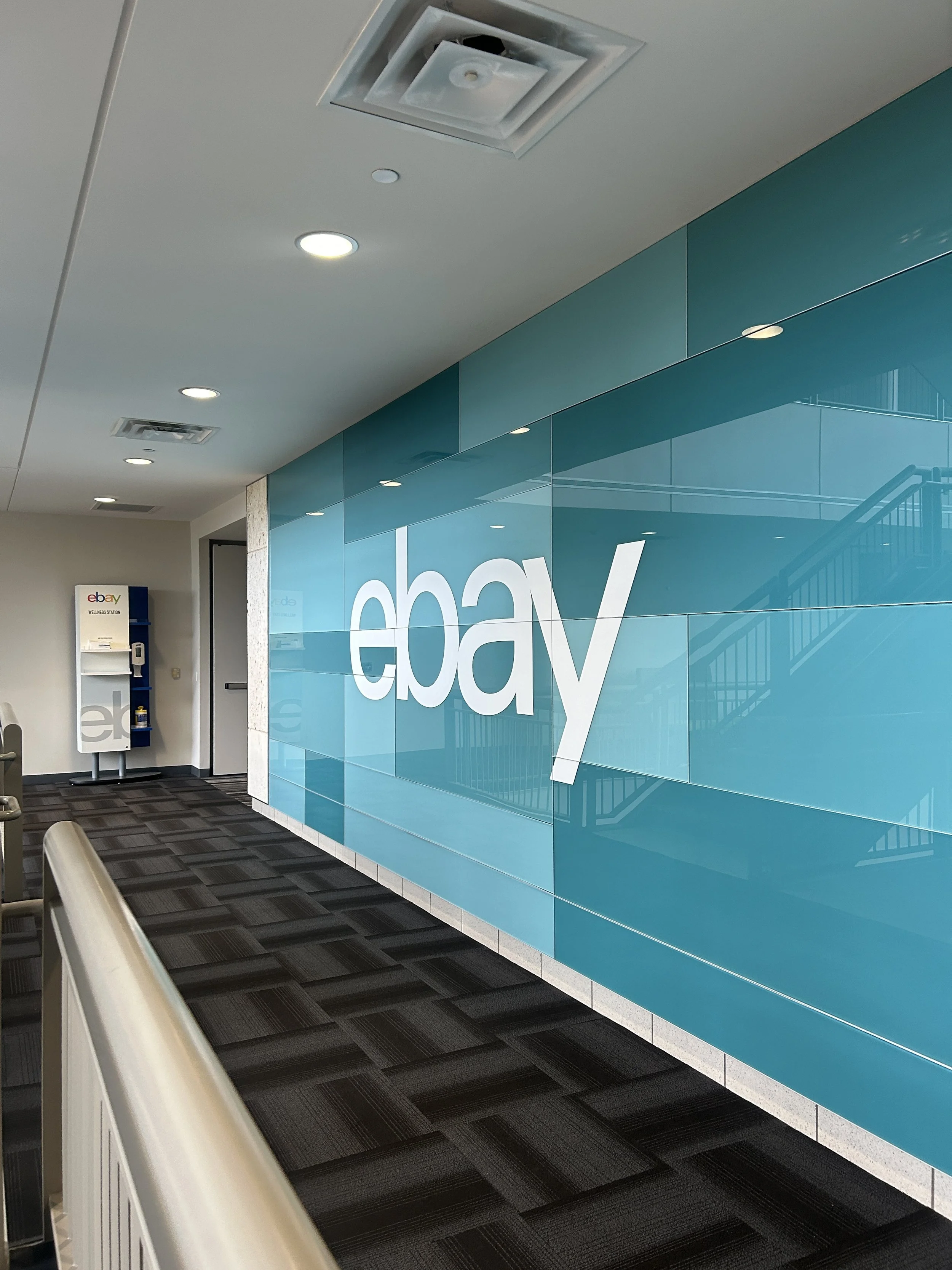 eBay Austin corridor wallcovering installation with layered teal graphics behind glass, featuring large white logo and full-length environmental branding.