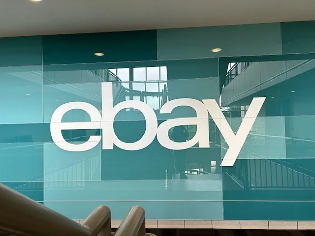 Installed eBay Austin wallcovering with teal graphic applied behind glass, featuring white logo and large-format environmental branding in office interior.