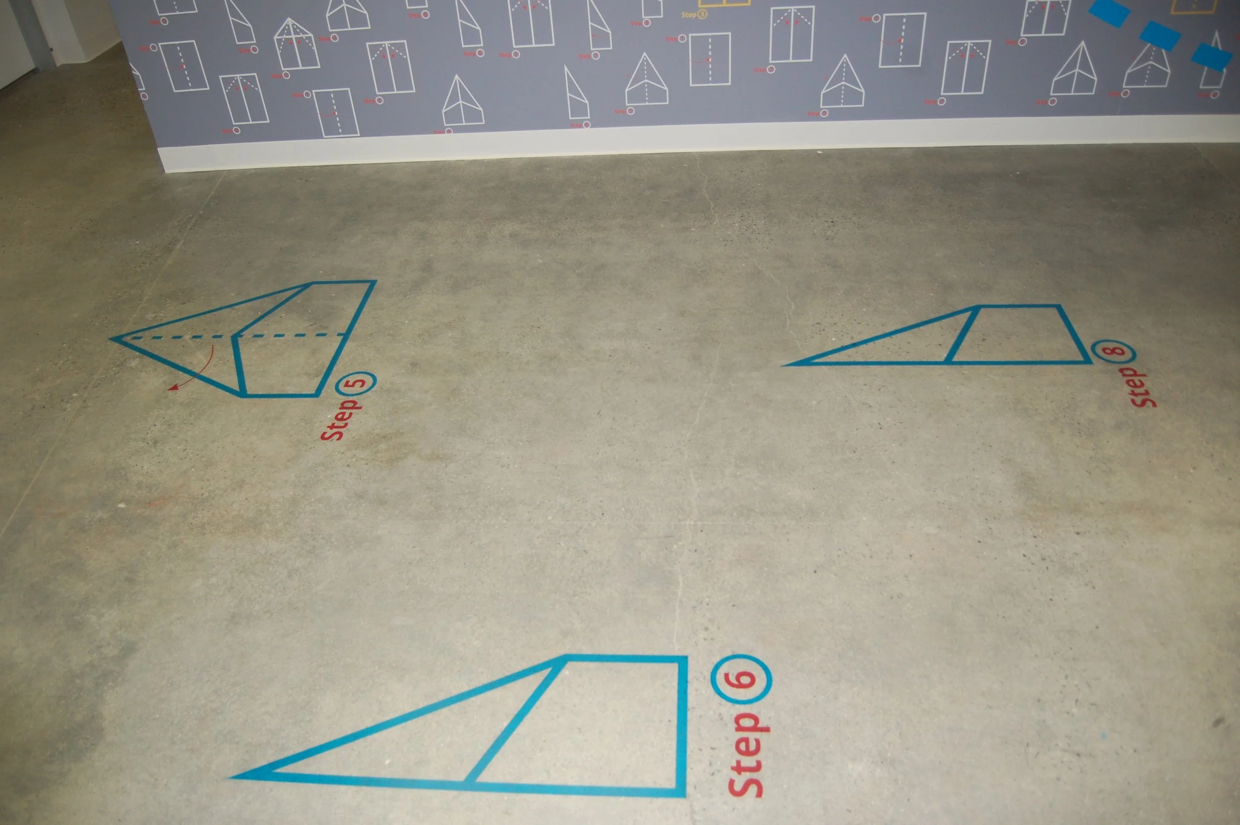 Paper plane floor graphics installed to create a playful wayfinding path in high-traffic commercial environment