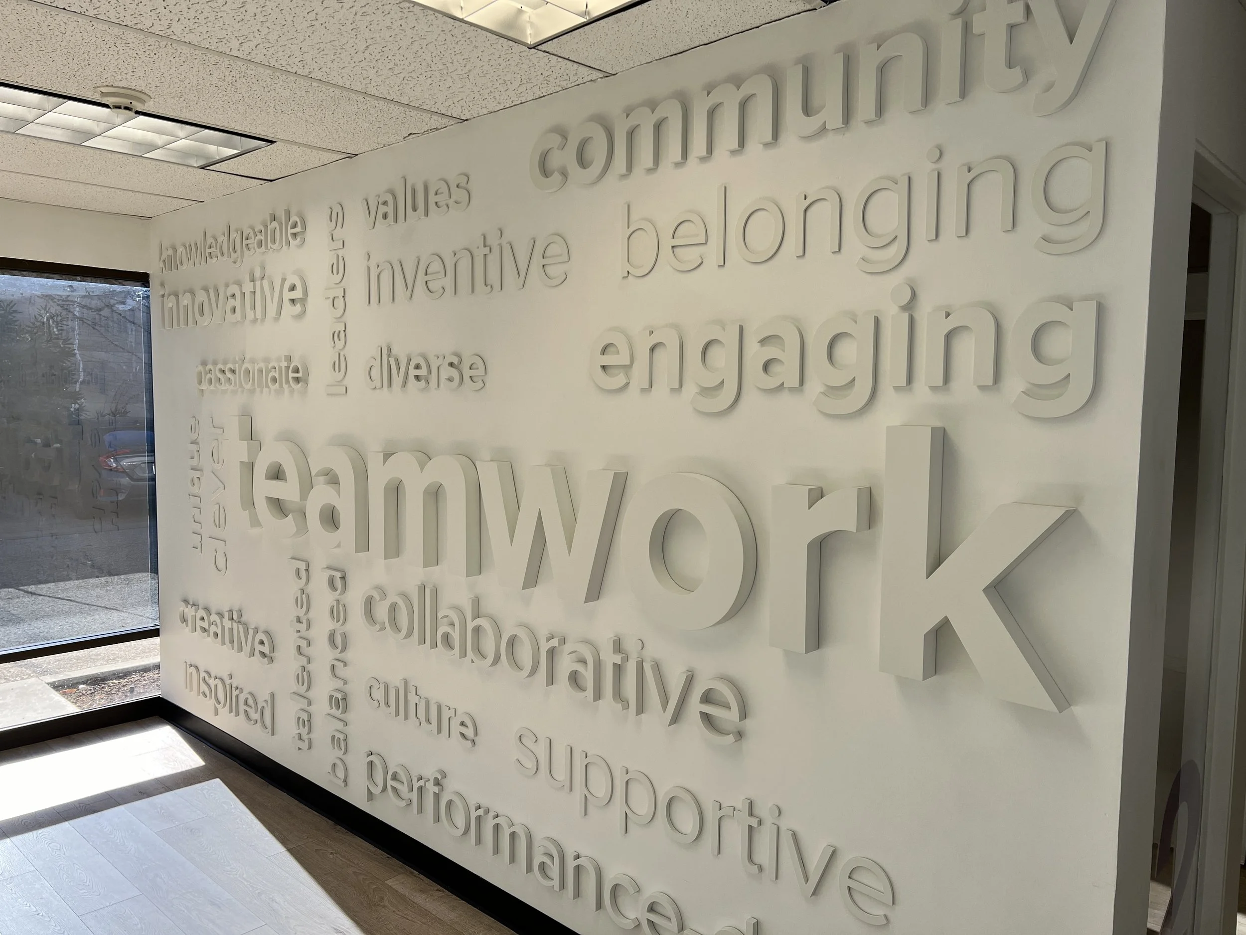 Dimensional typography environmental graphics feature wall showcasing brand messaging in corporate workspace