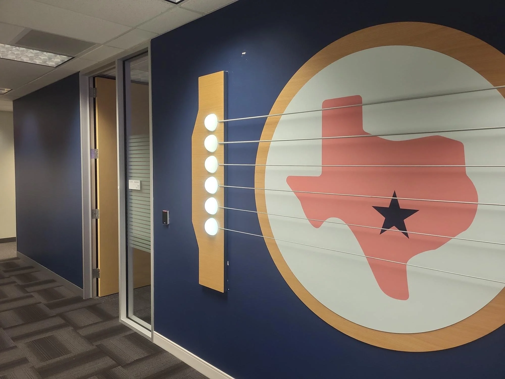 Installed eBay Austin dimensional wall feature showing Texas graphic with white oak surround, LED guitar elements, and branded environmental signage along office corridor.