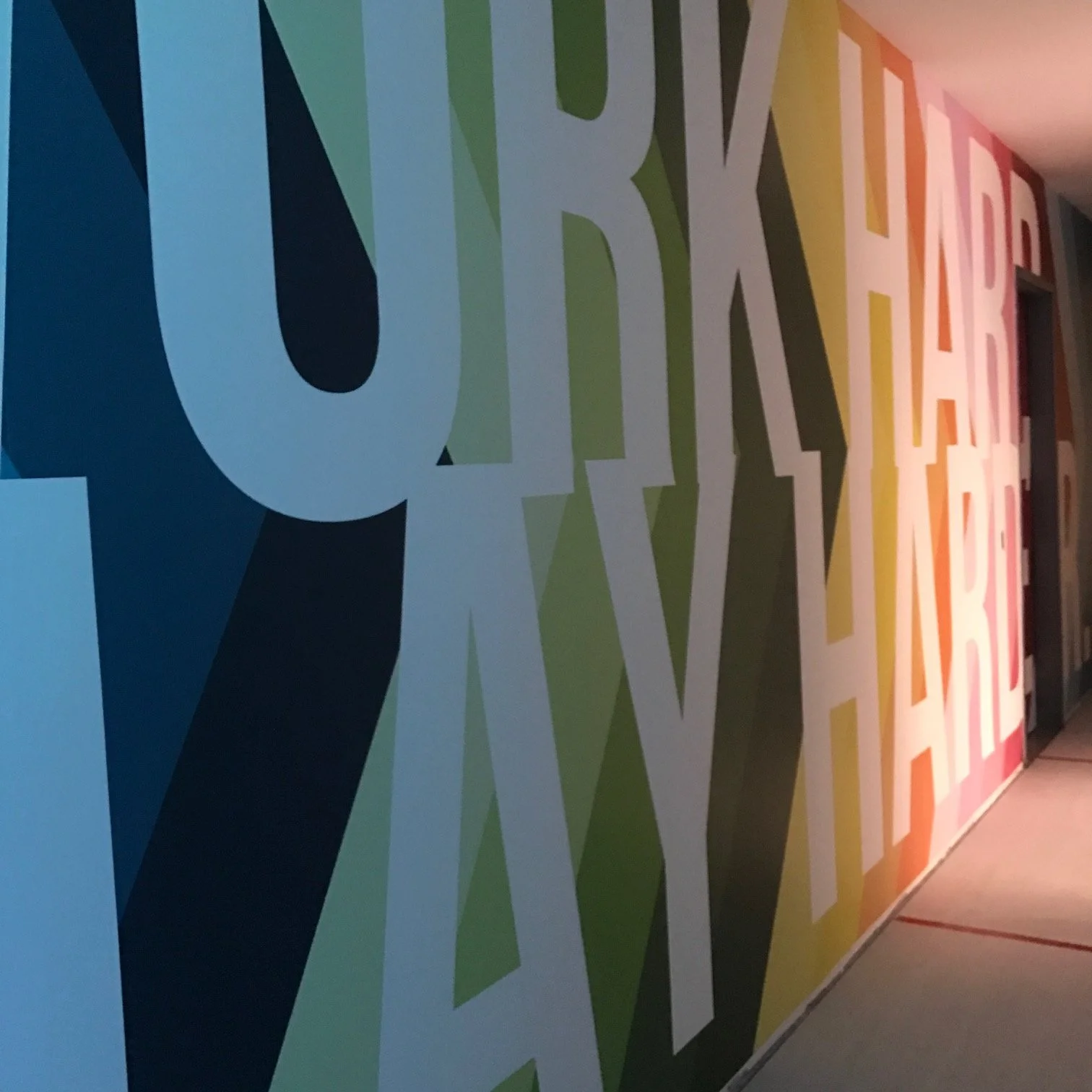 Large-scale branded typography wall graphic reinforcing company identity in a commercial interior.