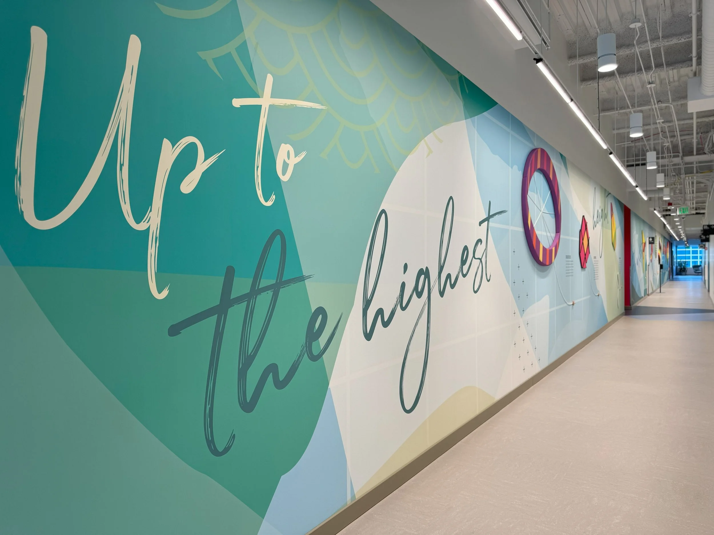 Large-scale corridor wall graphics with branded messaging designed to enhance workplace culture and visual engagement.