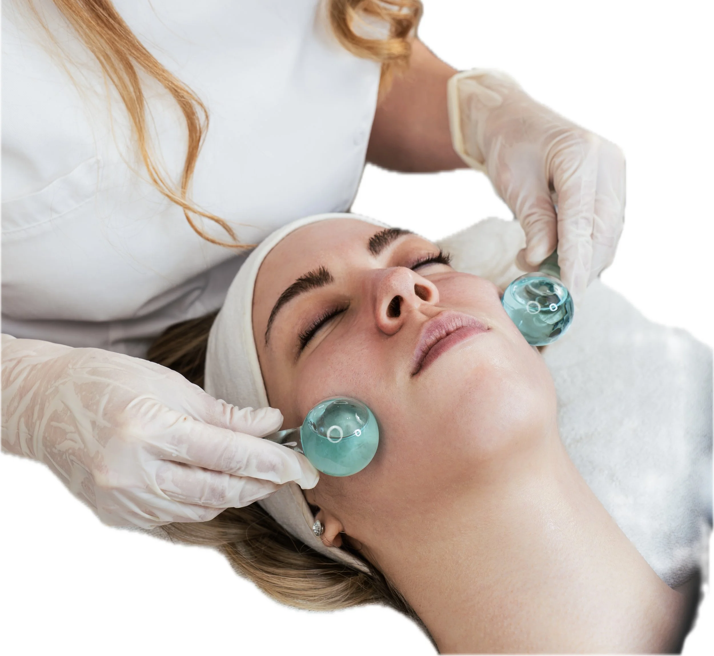 A woman receiving a facial treatment with jade roller tools on her cheeks in a spa setting.
