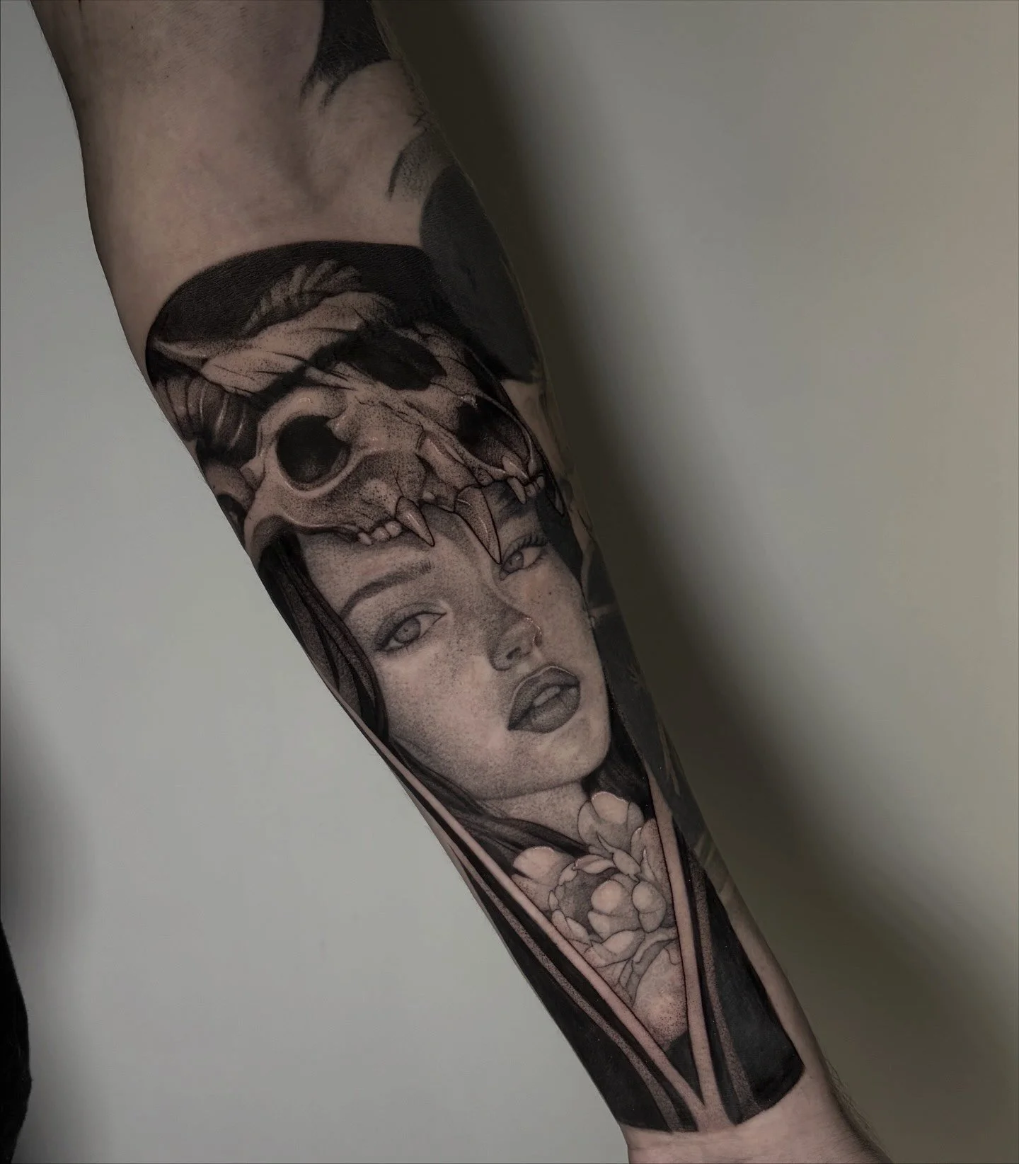 Tattoo eines Gesichts einer Frau mit offenen Lippen, ein Tierkopf und Blüten auf dem Unterarm.