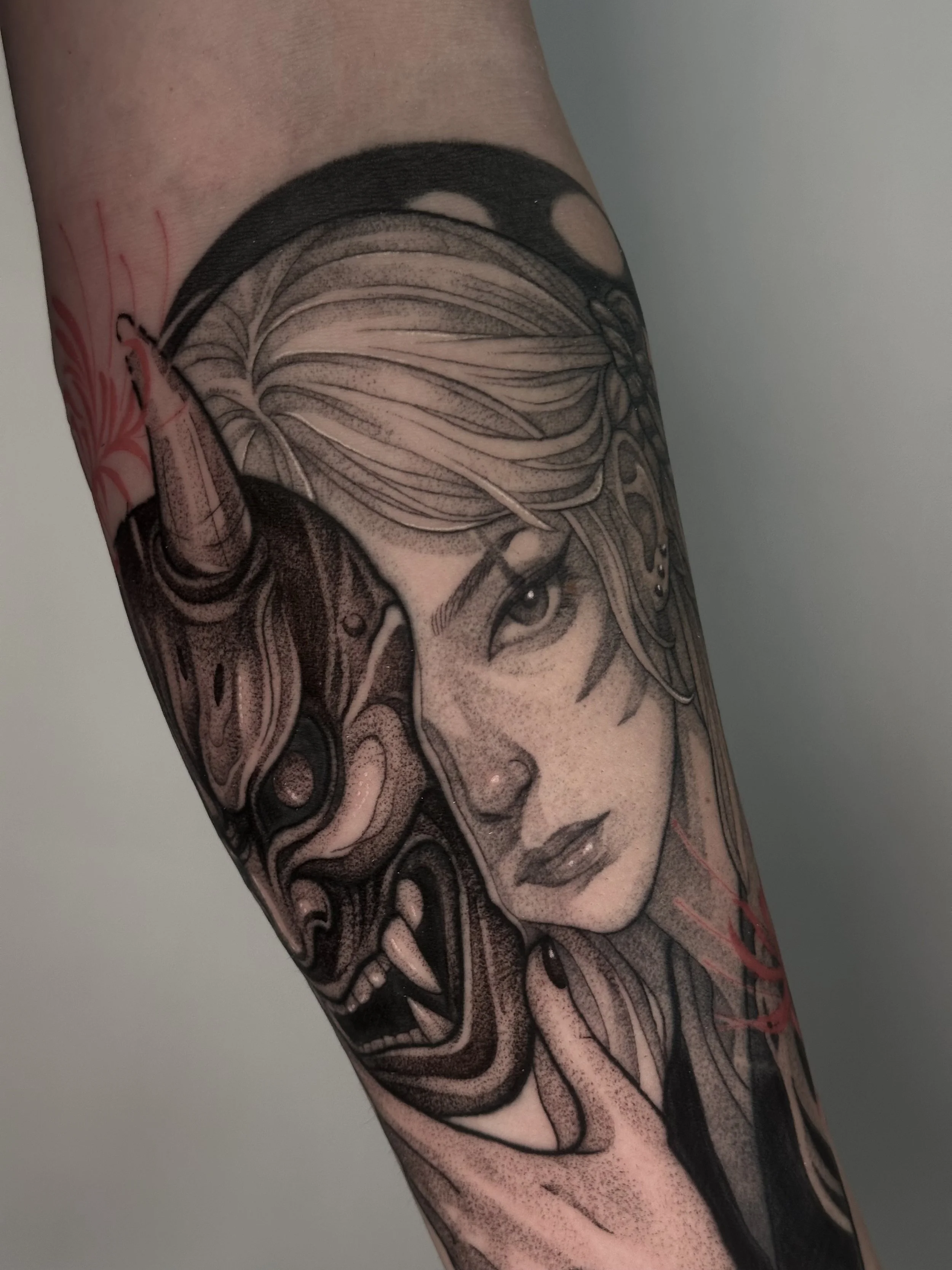 Tattoo eines detaillierten Porträts einer Frau mit blonder, welliger Frisur und blauen Augen, sowie einem dämonischen Gesicht mit offenen Mund und spitzen Zähnen auf dem Arm.