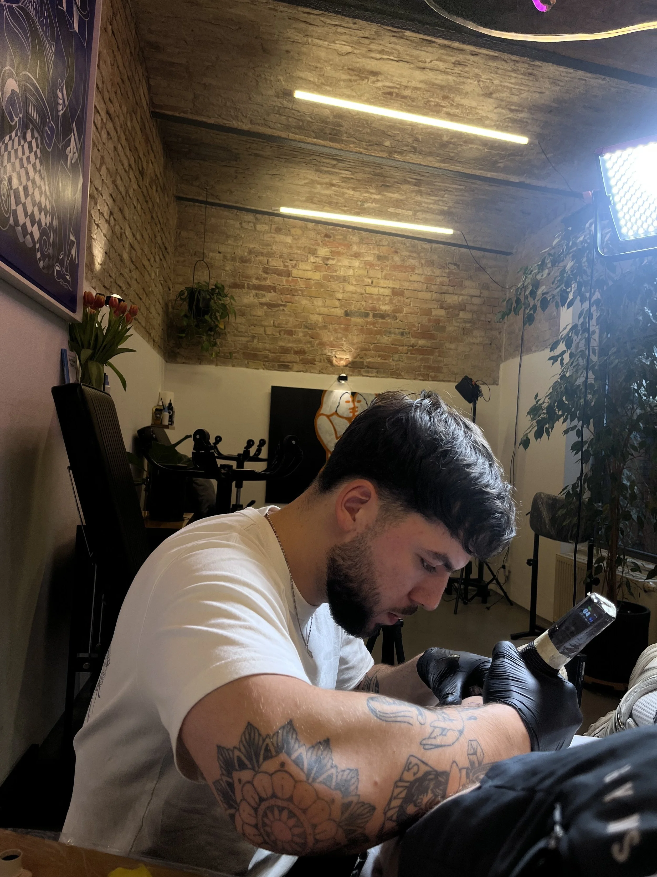 Mann mit Tattoo auf dem Arm, im Tattoo-Studio, Blick auf Smartphone, Tattoo wird gemacht.