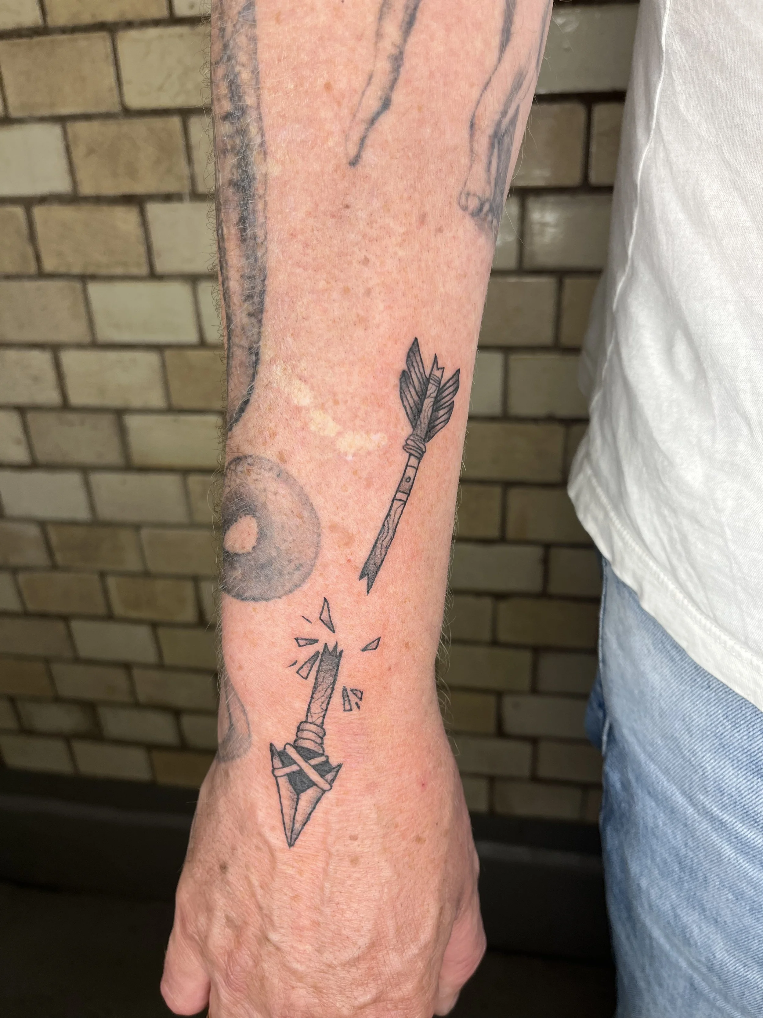 Tattoo eines zerbrochenen Pfeils auf dem Handgelenk einer Person.