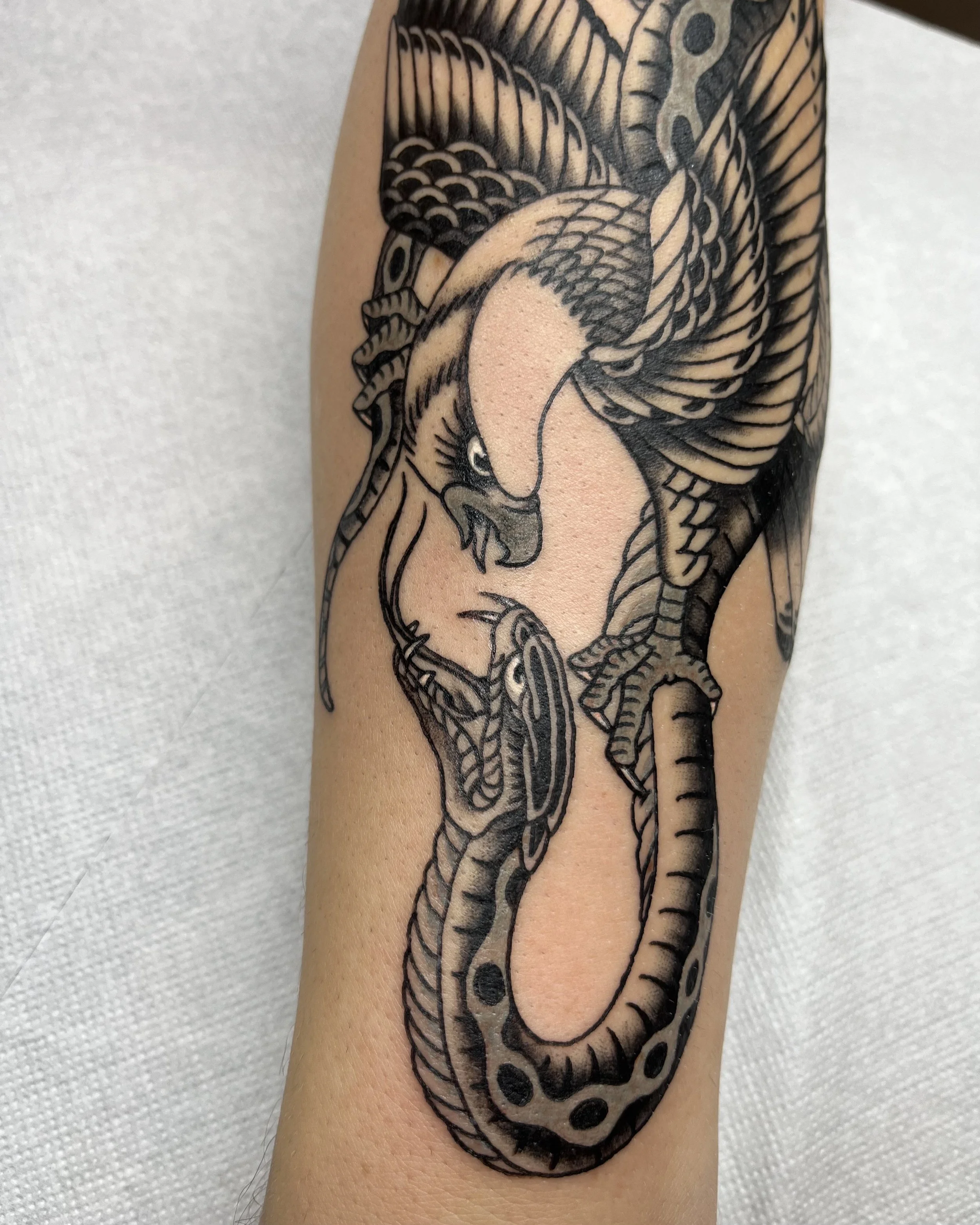 Schwarz-weiße Tätowierung eines Schlangen- und Adlermotivs auf einem Arm.