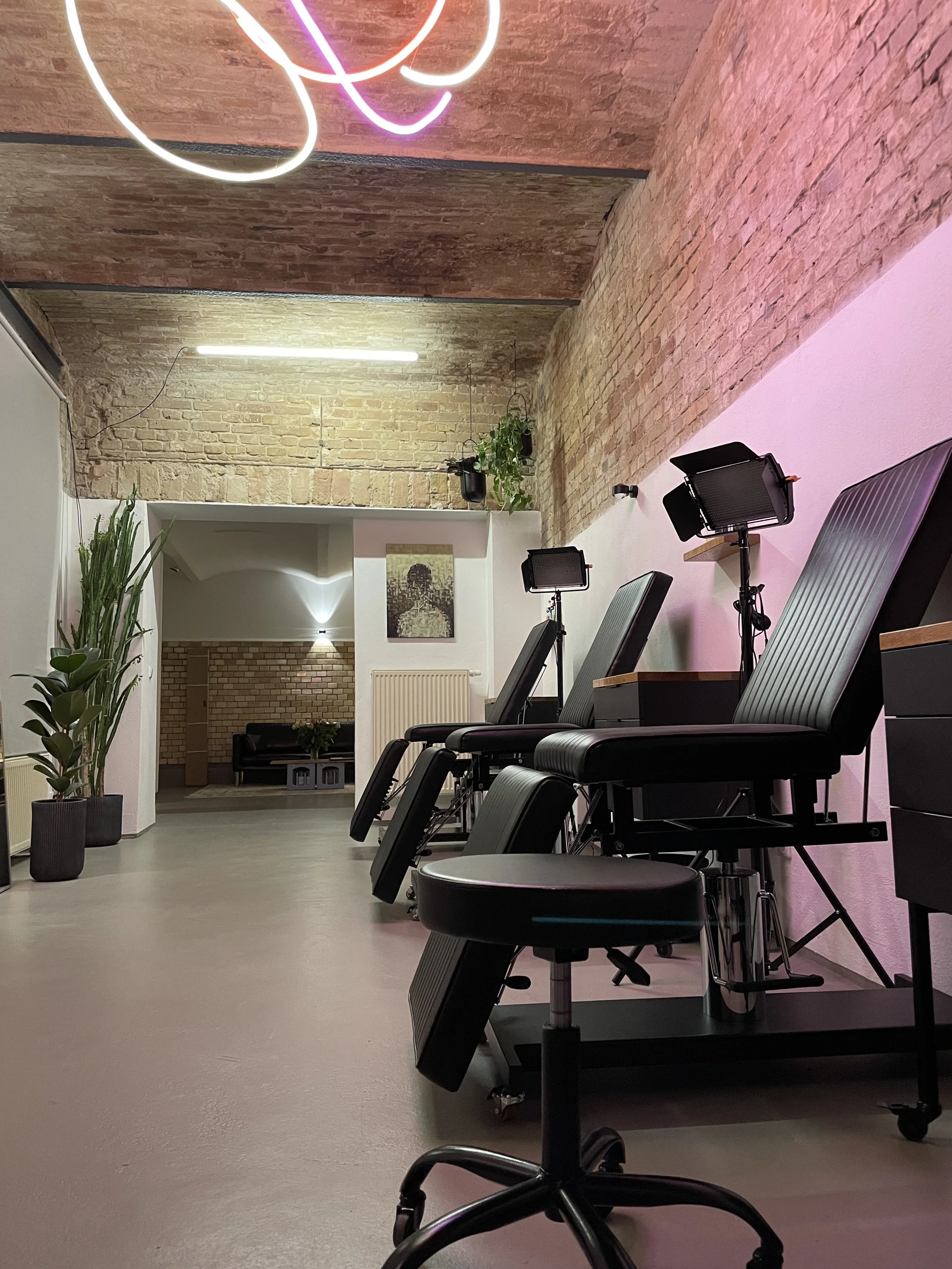 Innenaufnahme einer modernen Praxis oder Einrichtung mit Liegen, Pflanzen und Neon- und LED-Beleuchtung, Wand aus Backsteinen