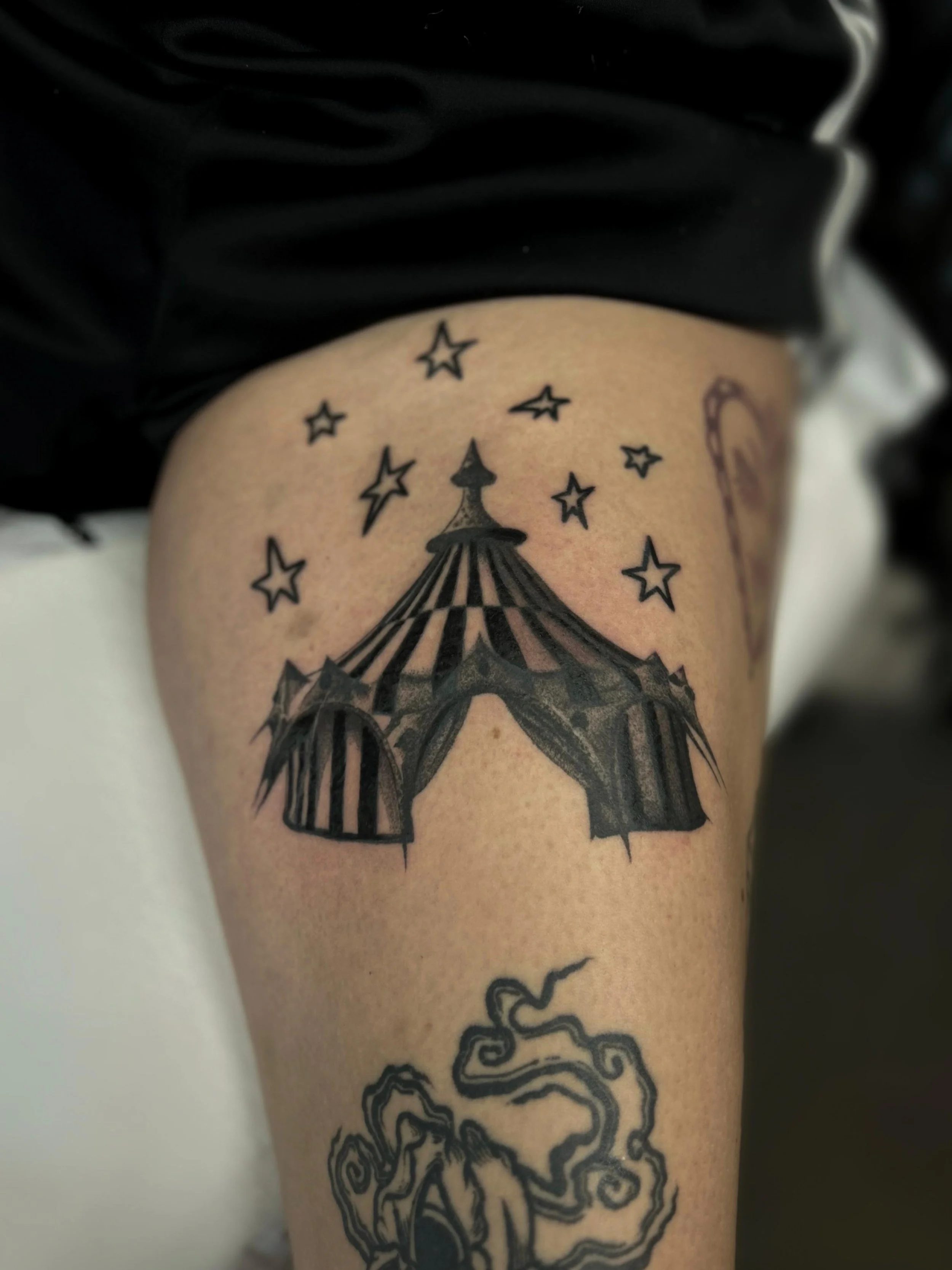 Tattoo eines großen Circus Zeltes mit Sternen darüber auf einem Oberschenkel