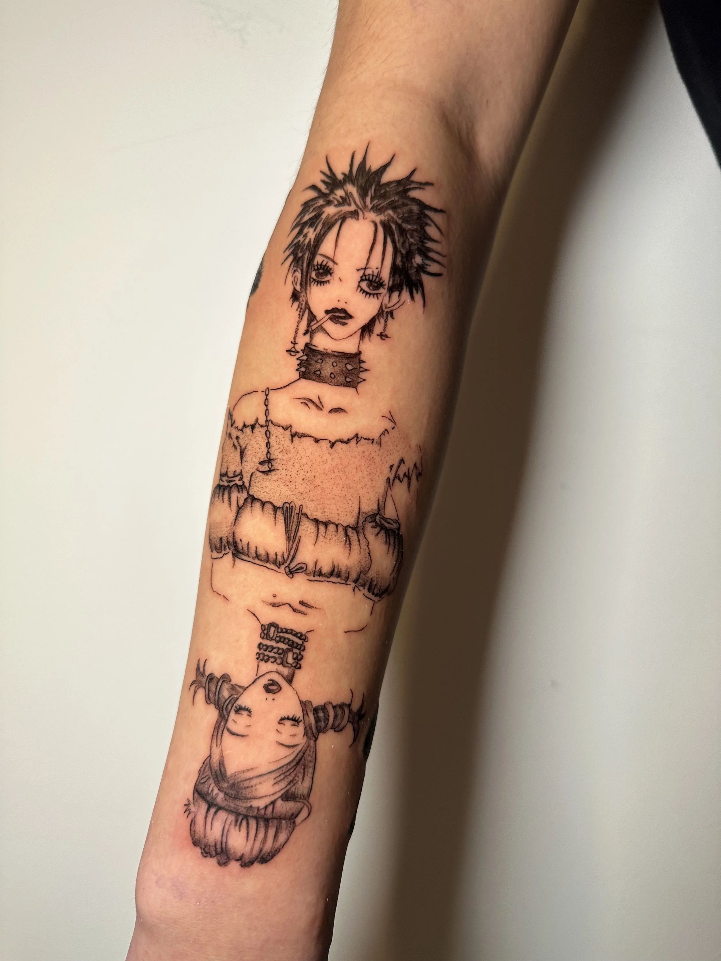 Tattoo eines weiblichen Gothic-Charakters mit spitzen Haaren, dunklem Make-up und Piercings, auf dem Unterarm.