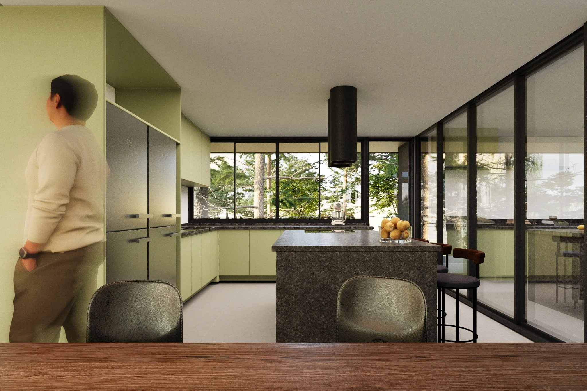 Modern kitchen with light green cabinets, black countertops, a central island with a bowl of apples, a coffee machine, large windows with trees outside, and a person leaning against the wall.