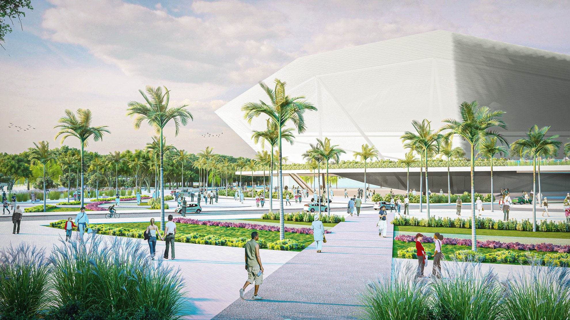 Public park with walking paths, palm trees, colorful flower beds, and a modern architectural building in the background, with people walking, cycling, and gathering.
