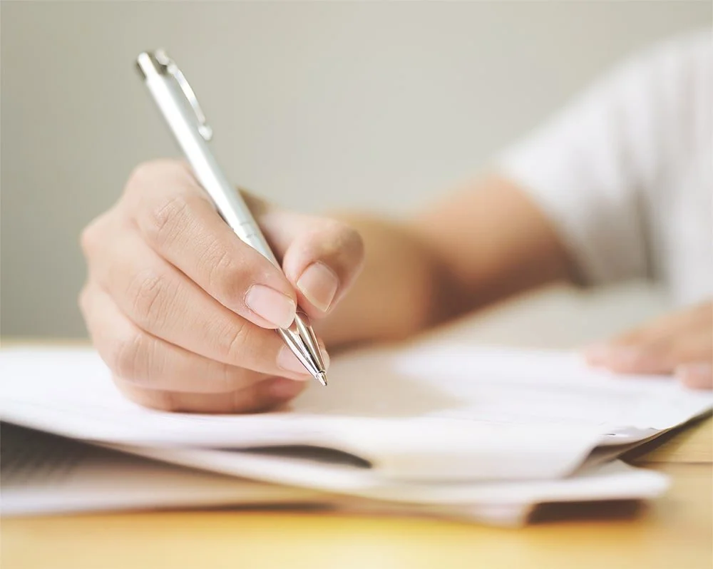 Close-up of a person writing with a silver pen on paper.
