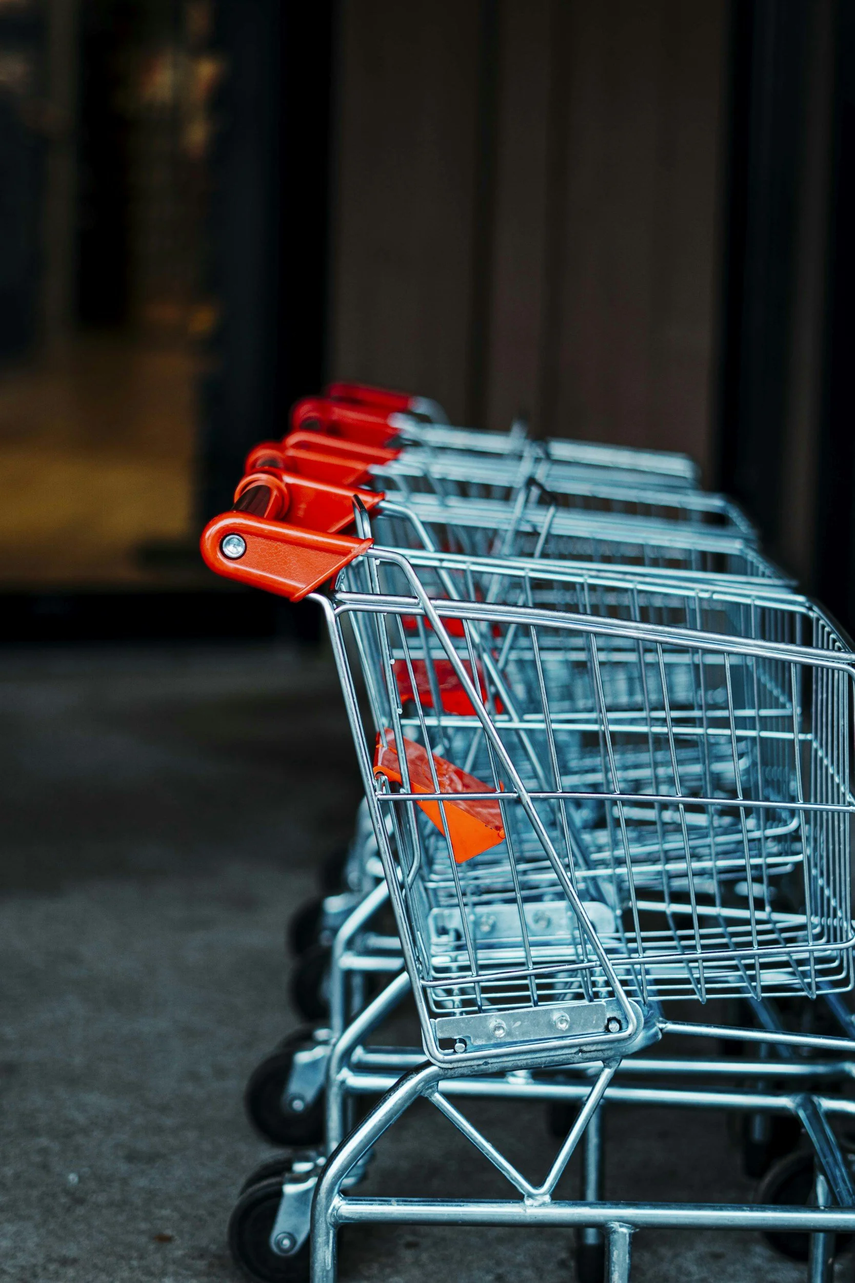A row of empty shopping carts with red handles lined up outside a store.