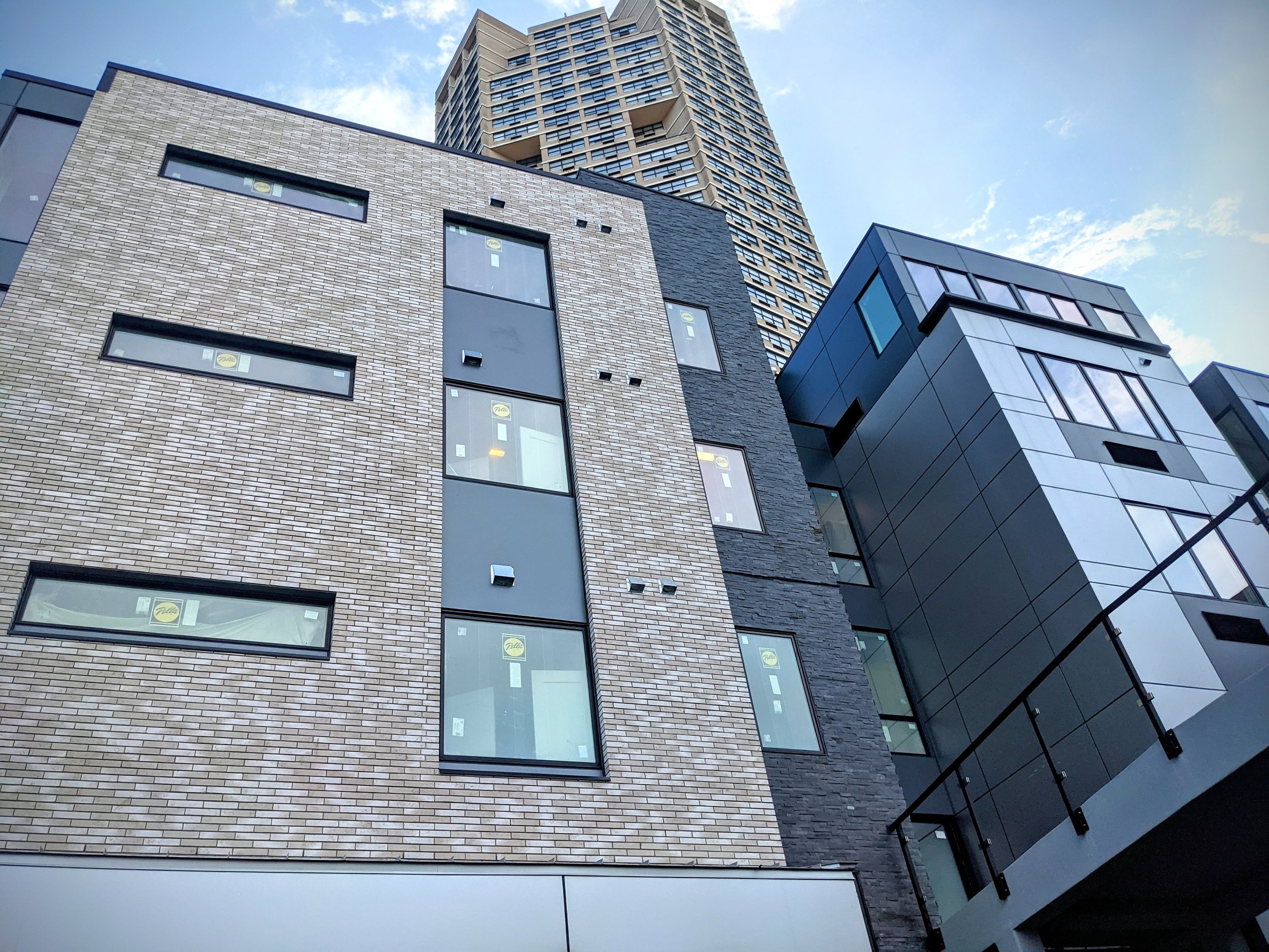Low-angle view of modern multi-story buildings with brick, dark panel, and glass exteriors in an urban setting during daytime.