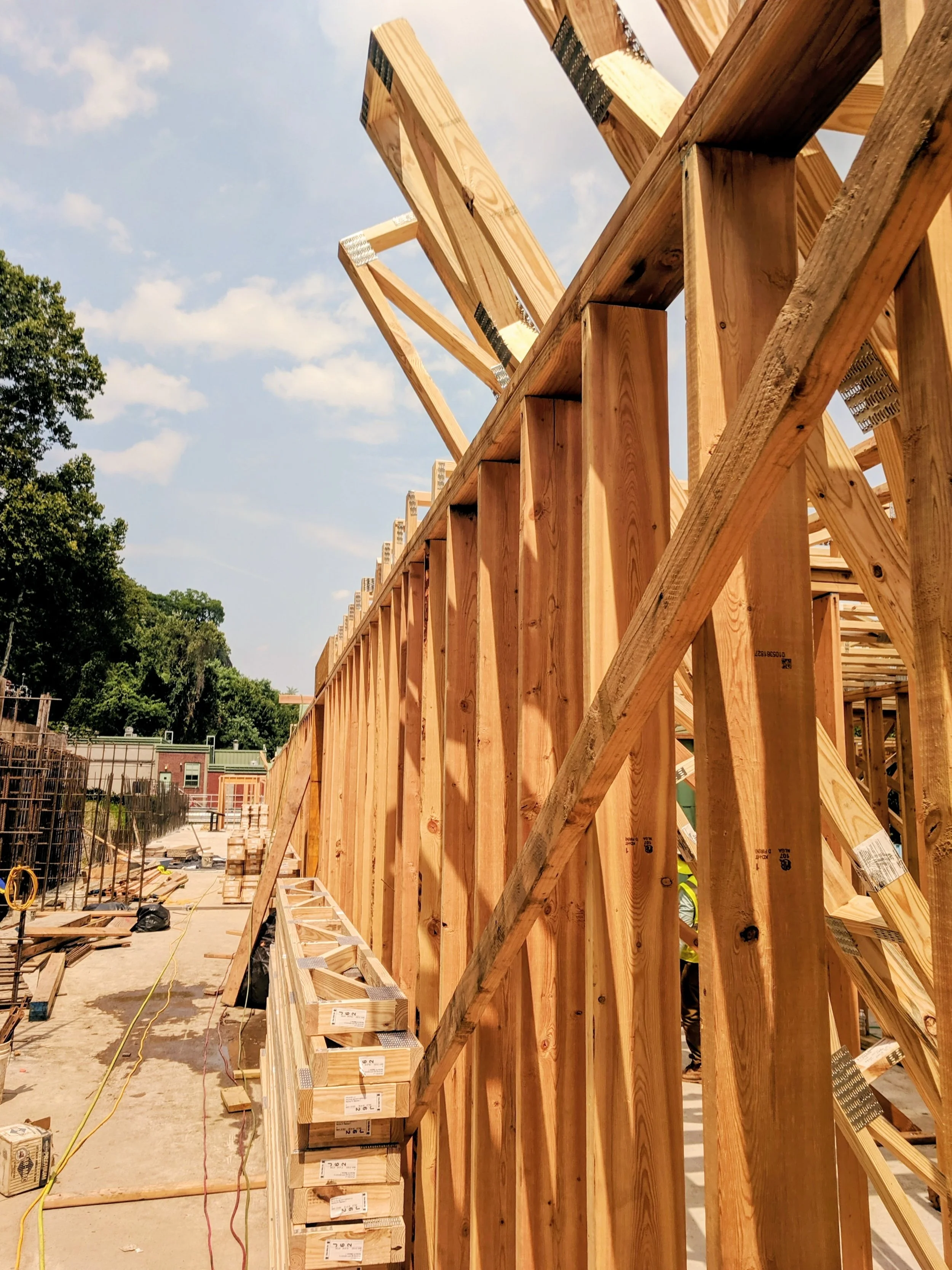 Wooden framing for a building under construction with a partly cloudy sky and trees in the background.