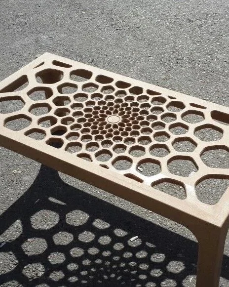 A beige bench with a honeycomb pattern on the seat, casting a shadow with similar honeycomb shapes onto the ground.