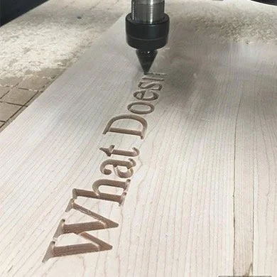 A CNC machine engraving the words 'What Does' into a wooden surface.