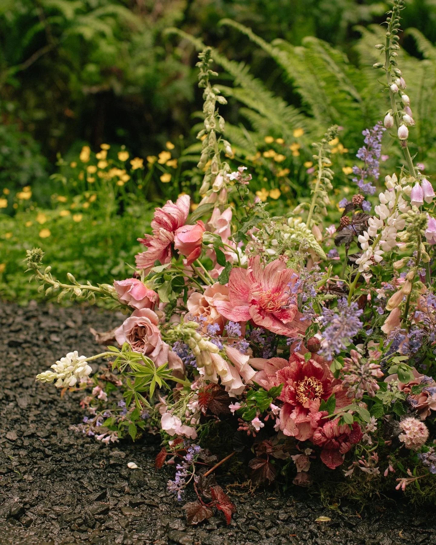 A colorful arrangement of pink, purple, and white flowers on the ground with a park or garden background of green foliage and small yellow flowers.