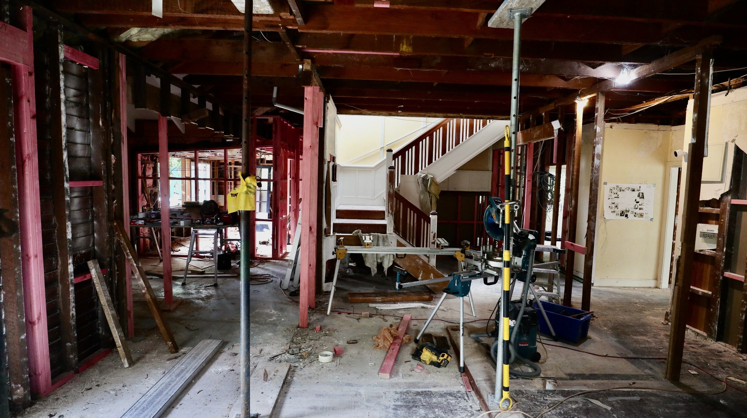 Interior of a house under renovation with exposed framing, construction tools, and equipment scattered around.