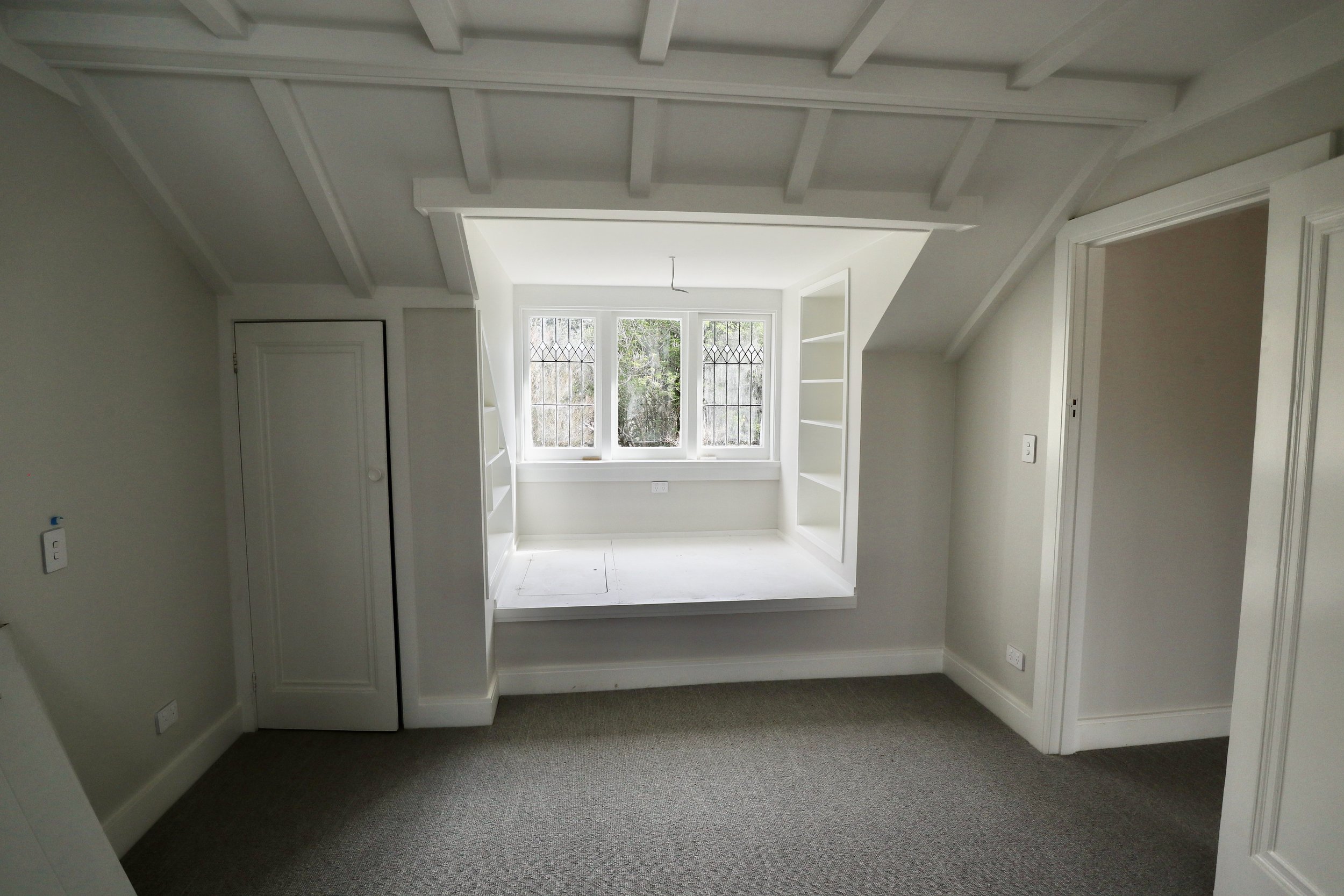 Empty room with a window seat, built-in shelves on either side, and a skylight above.
