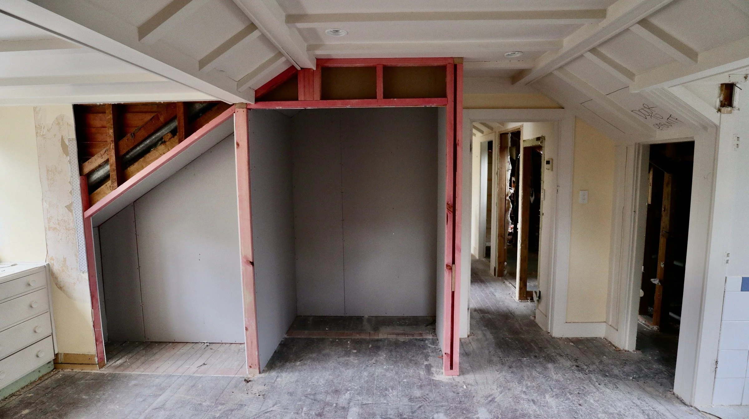 Interior of a house under renovation, with exposed wall framing, partially finished drywall, and construction debris on the floor.