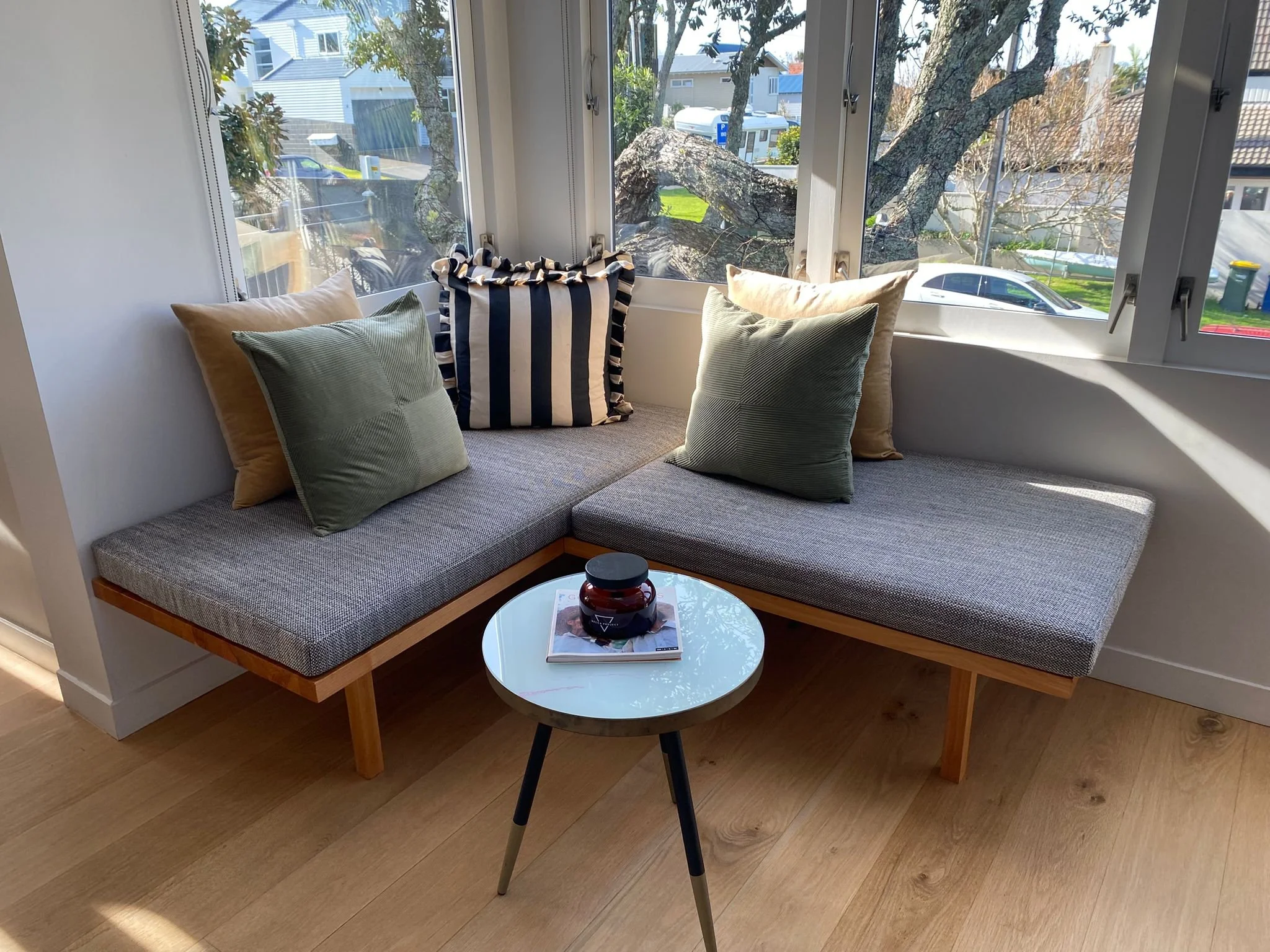A cozy bay window nook with a modern gray cushion upholstered bench with wooden legs.