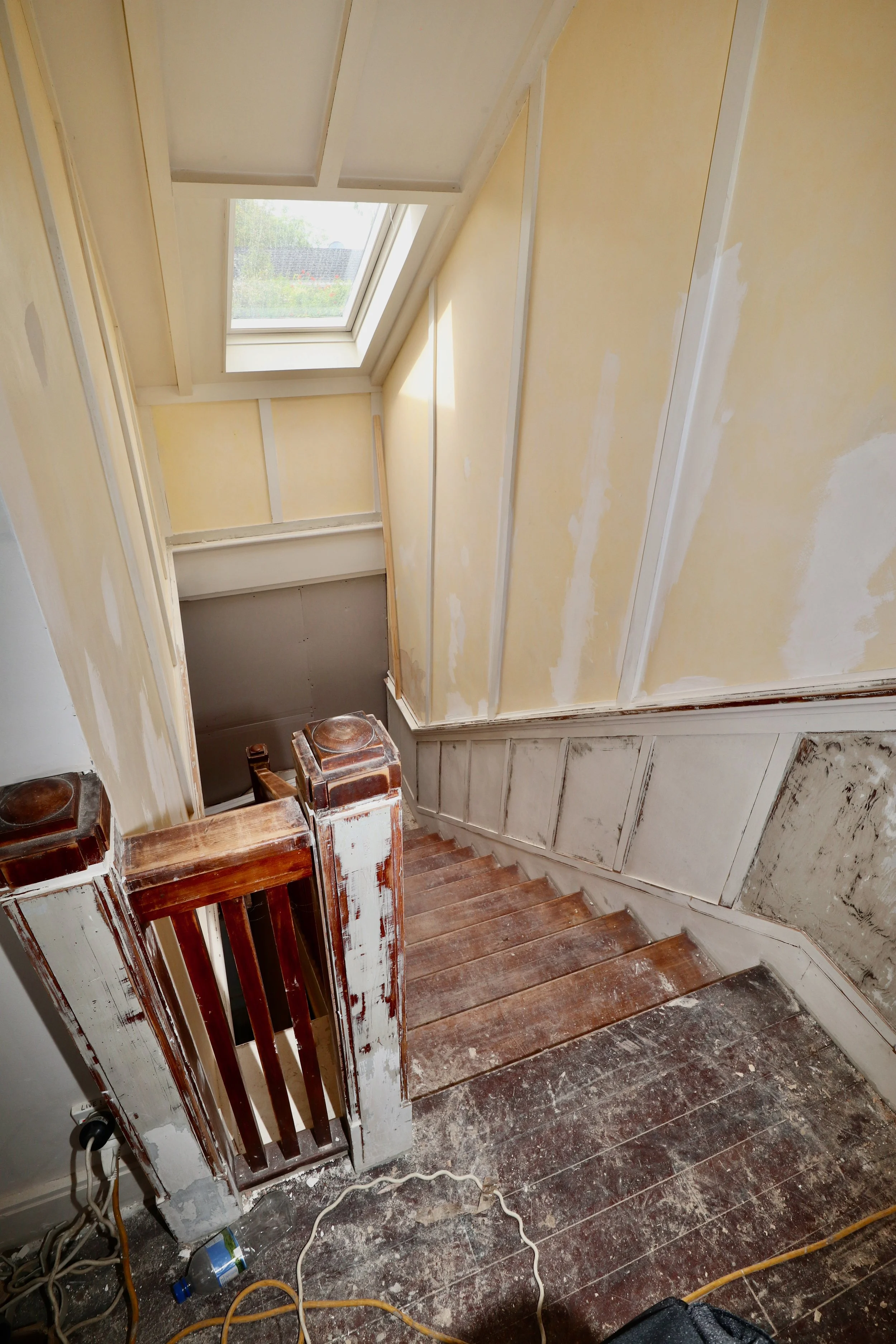 View of a staircase under renovation with unfinished walls, in a space with a skylight window, and construction tools and debris on the floor.