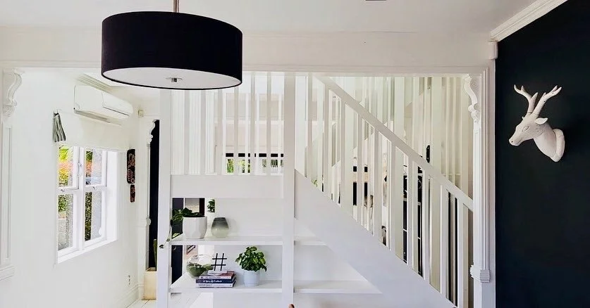 Bright living room with white walls, a staircase, black and white decor, and a white deer head wall ornament.