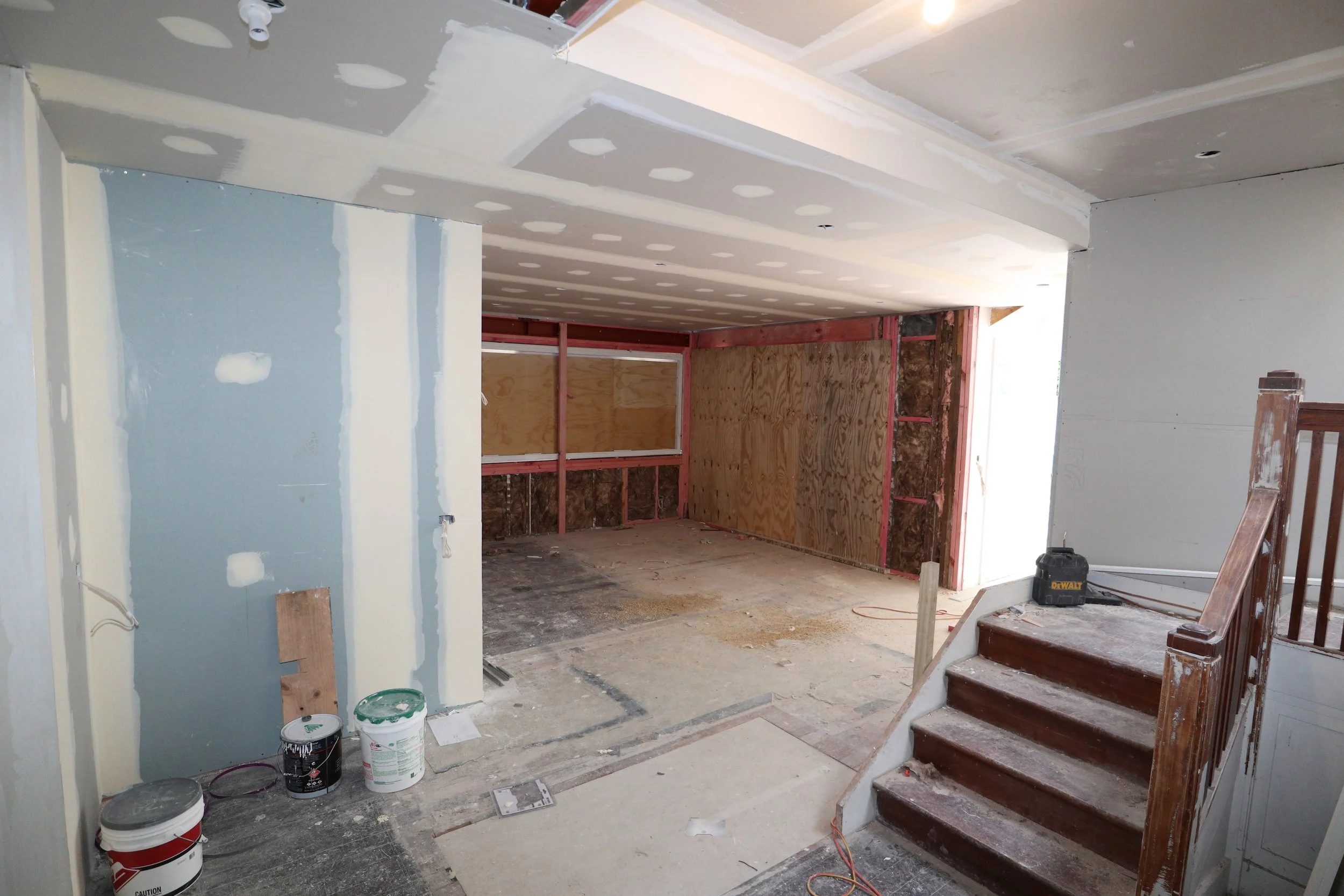 Interior of a house under construction with unfinished walls, drywall, and wooden staircase.