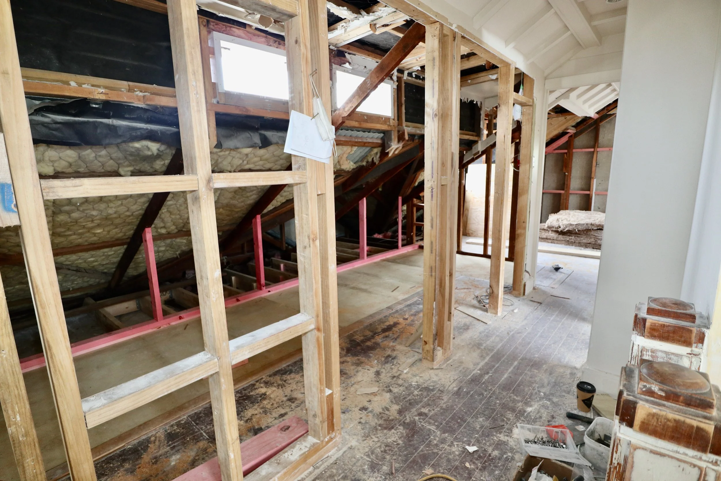 Interior of a house under renovation with exposed wooden framing, insulation, and construction tools on the floor.