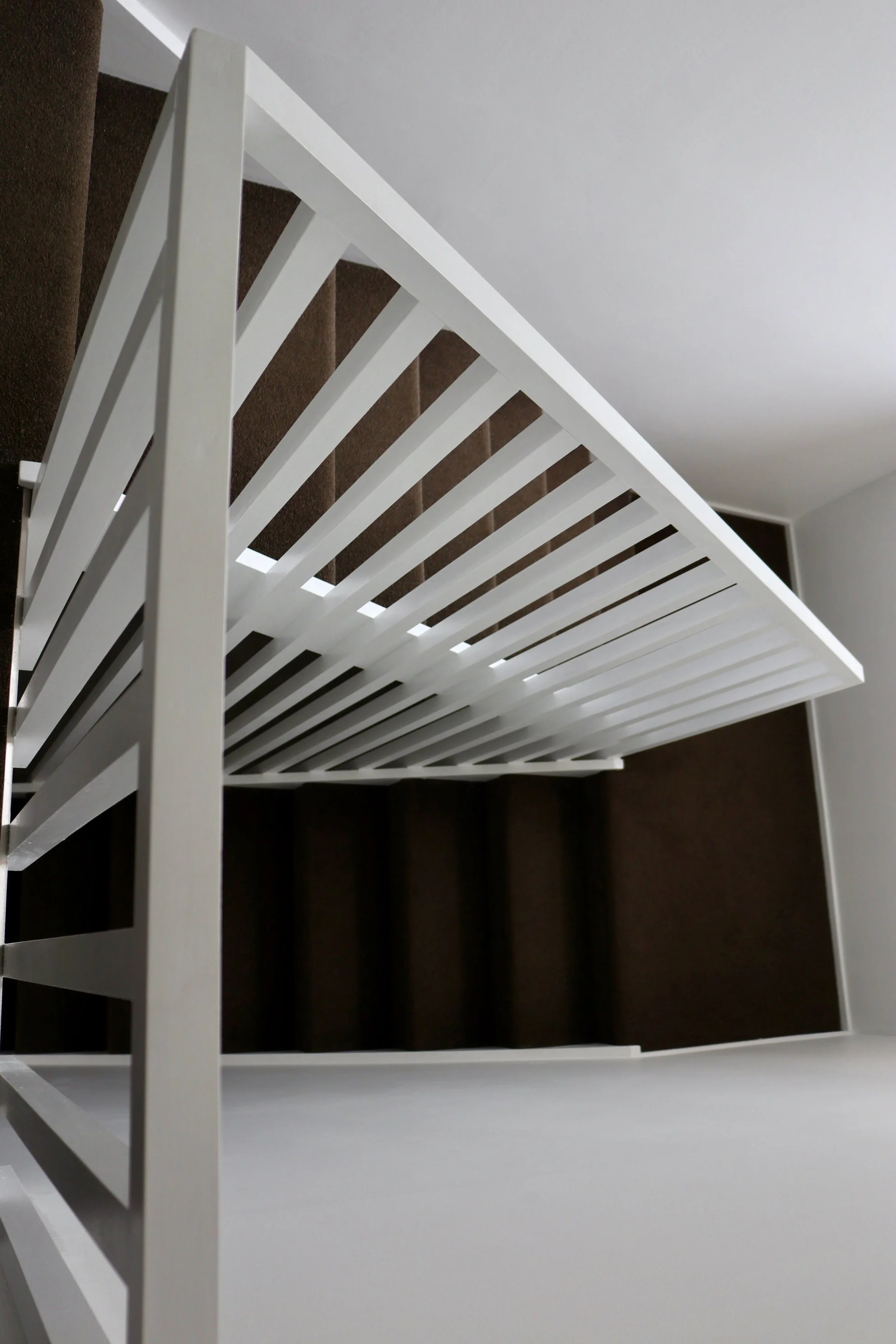 White metal shoe rack placed on a combination of brown carpeted and white flooring.