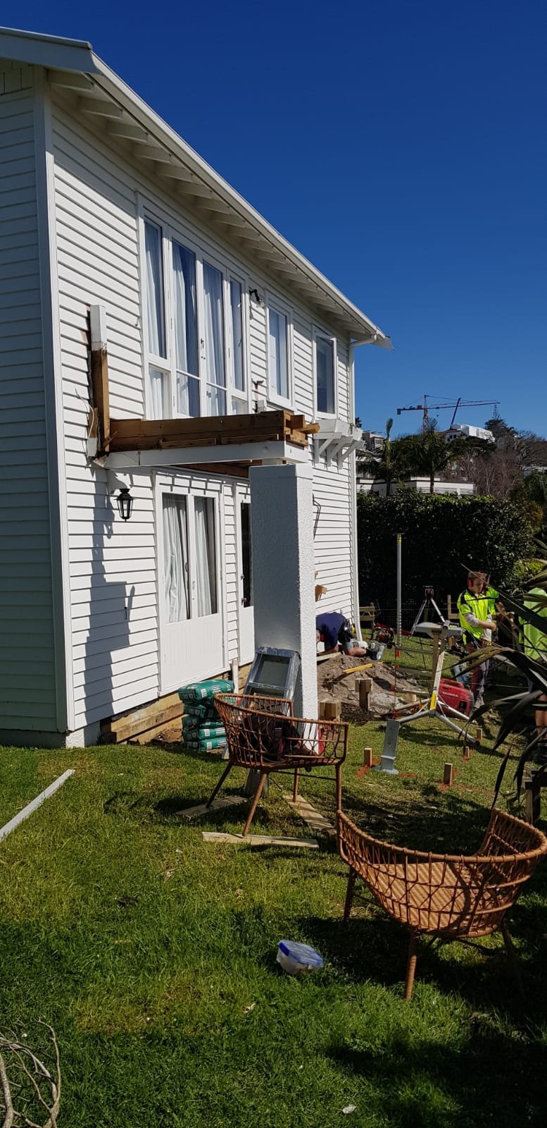 Side view of a white house under construction with workers on site and tools scattered around.