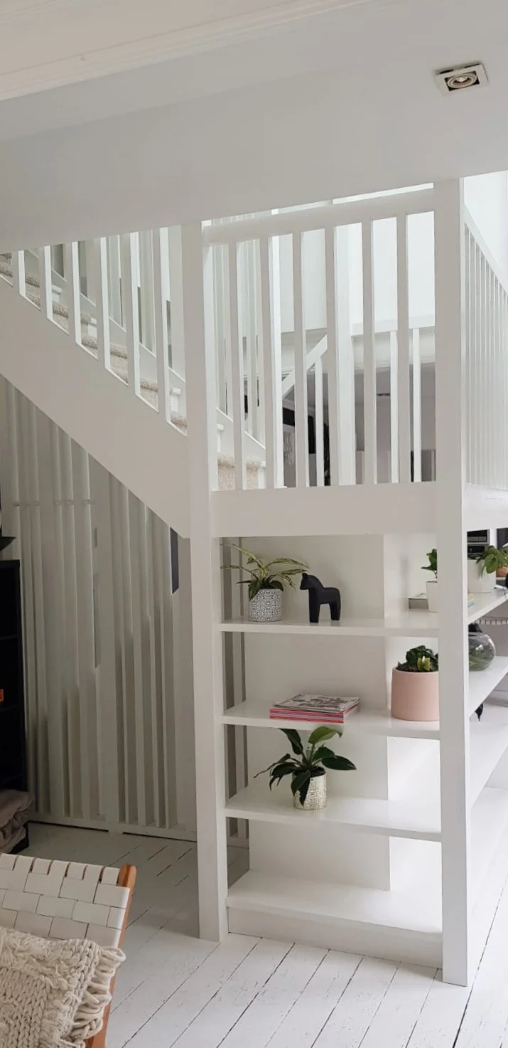 White staircase with vertical balusters and built-in shelves decorated with potted plants, a black horse figurine, and magazines in a modern, indoor residential space.
