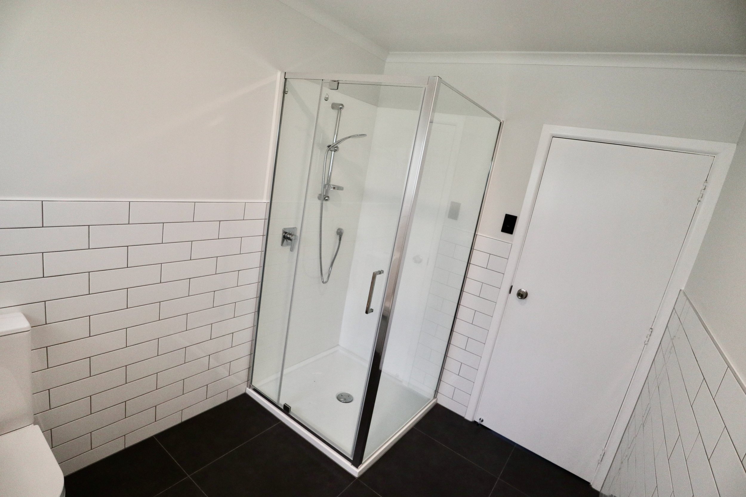Modern bathroom with a glass shower enclosure, white tiled walls, and black floor tiles.